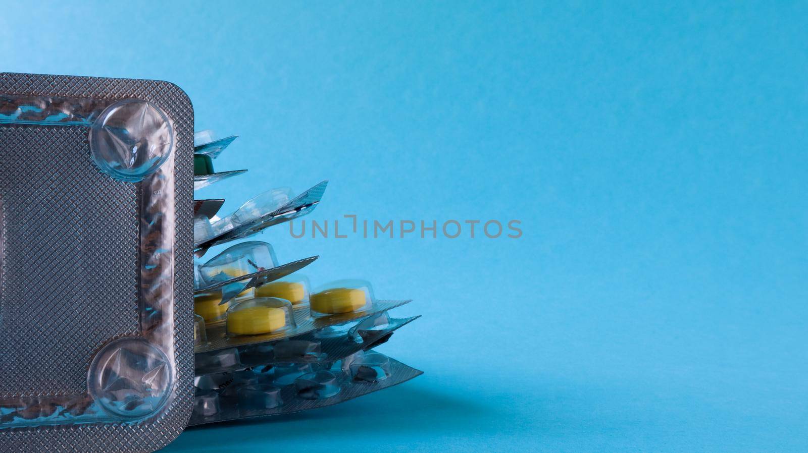 Packs of pills of various shapes and colors are stacked on a blue background. Capsules are packaged in blister packs. Different medicines. Drug treatment. Health photo. Copy space