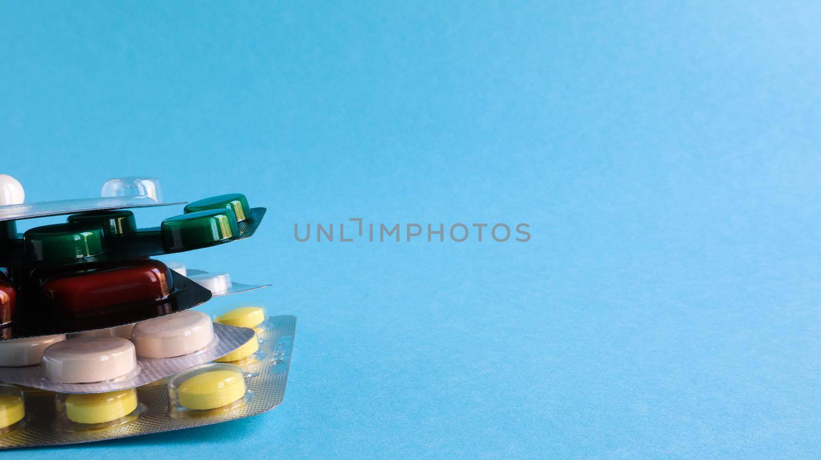 Packs of pills of various shapes and colors are stacked on a blue background. Capsules are packaged in blister packs. Different medicines. Drug treatment. Health photo. Copy space