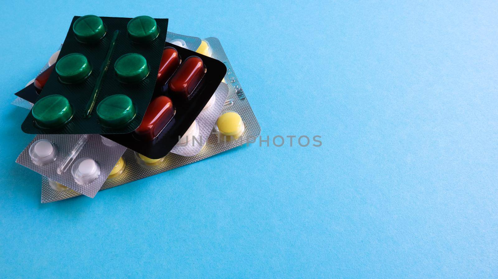 Packs of pills of various shapes and colors are stacked on a blue background. Capsules are packaged in blister packs. Different medicines. Drug treatment. Health photo. Copy space