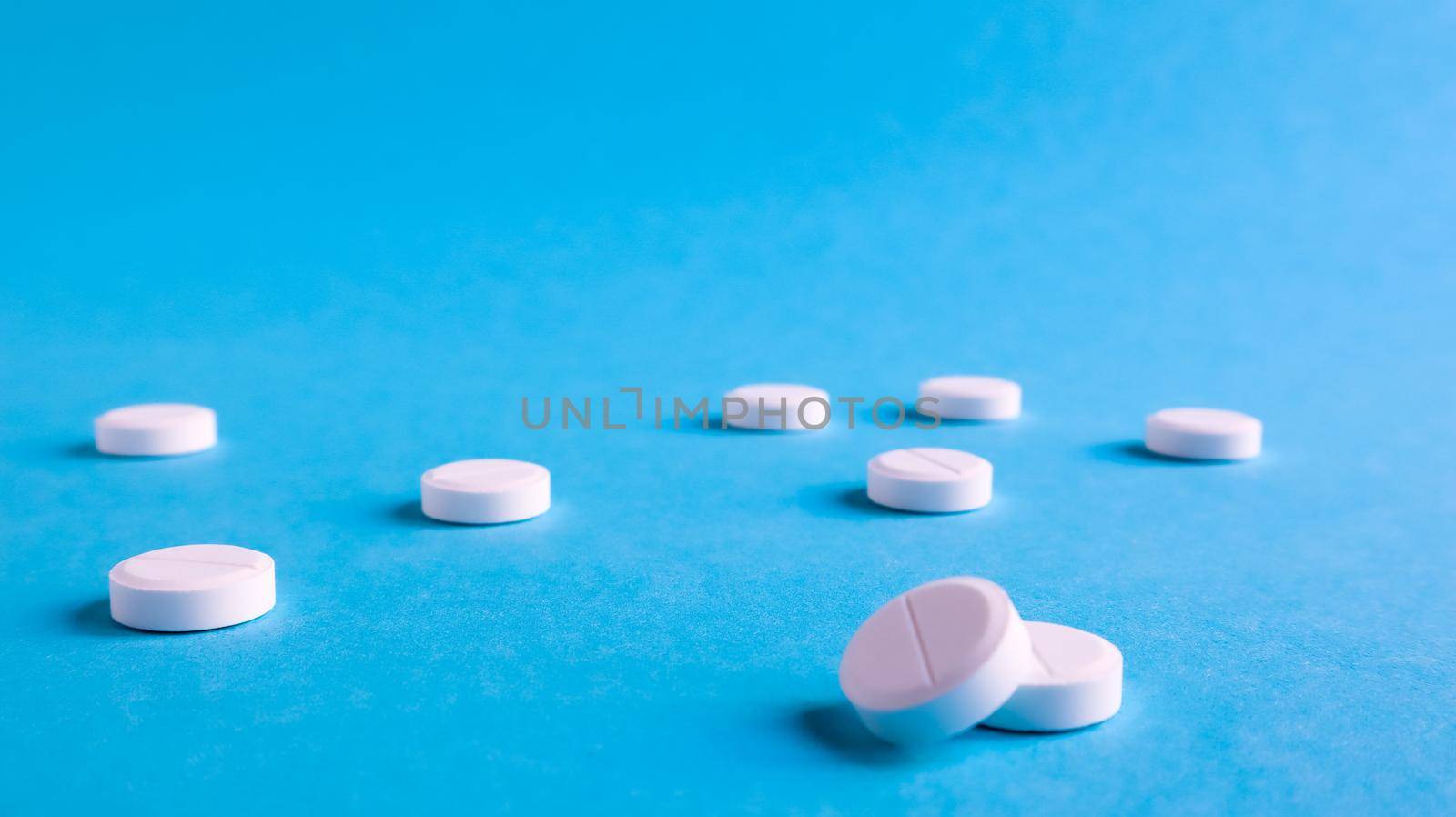 White round medical pills on a blue background. Scattered white pills on the table. The concept of medicine, pharmacy and healthcare. Copy space Empty space for text or logo