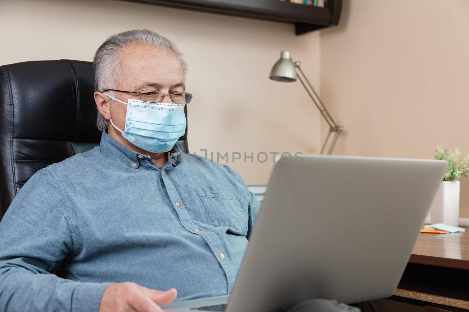 senior man in face mask working or communicate on laptop at home. study, training, work, communication, entertainment, leisure during the coronavirus period. by lunarts