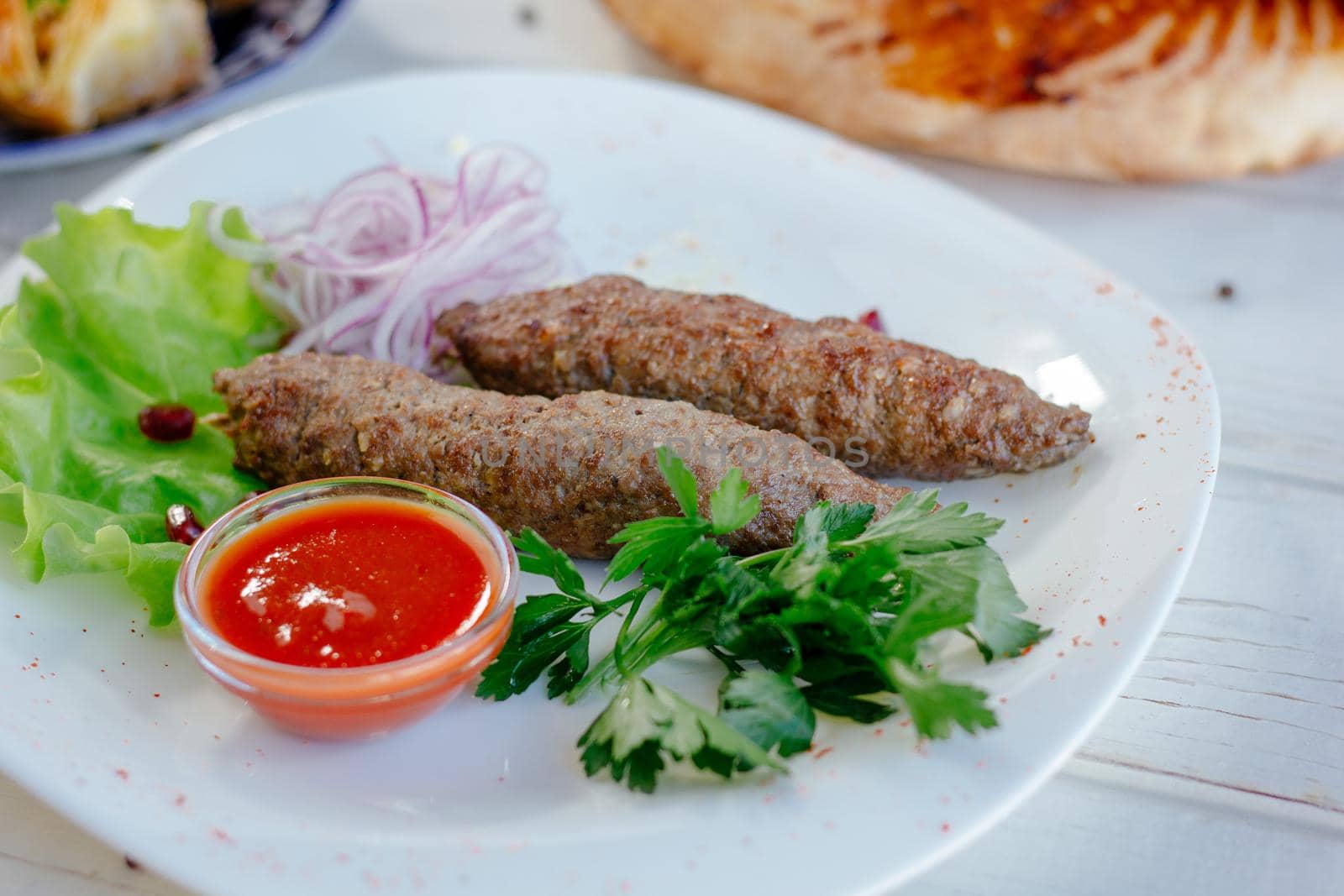 Meat kebabs on white plate with green herbs and red sauce, great image for your needs.