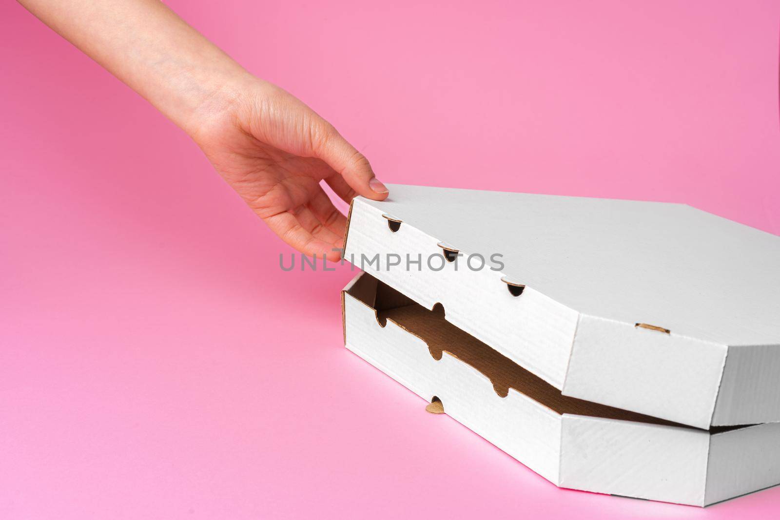 Female hand opening pizza delivery box on pink background. Food delivery