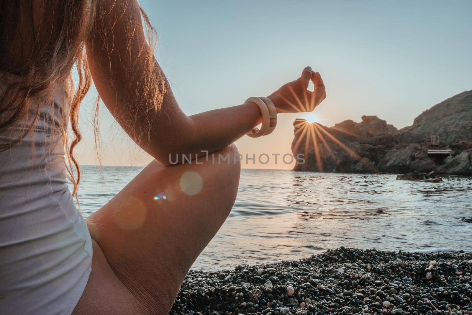 Young woman in swimsuit with long hair practicing stretching outdoors on yoga mat by the sea on a sunny day. Women's yoga fitness pilates routine. Healthy lifestyle, harmony and meditation concept.