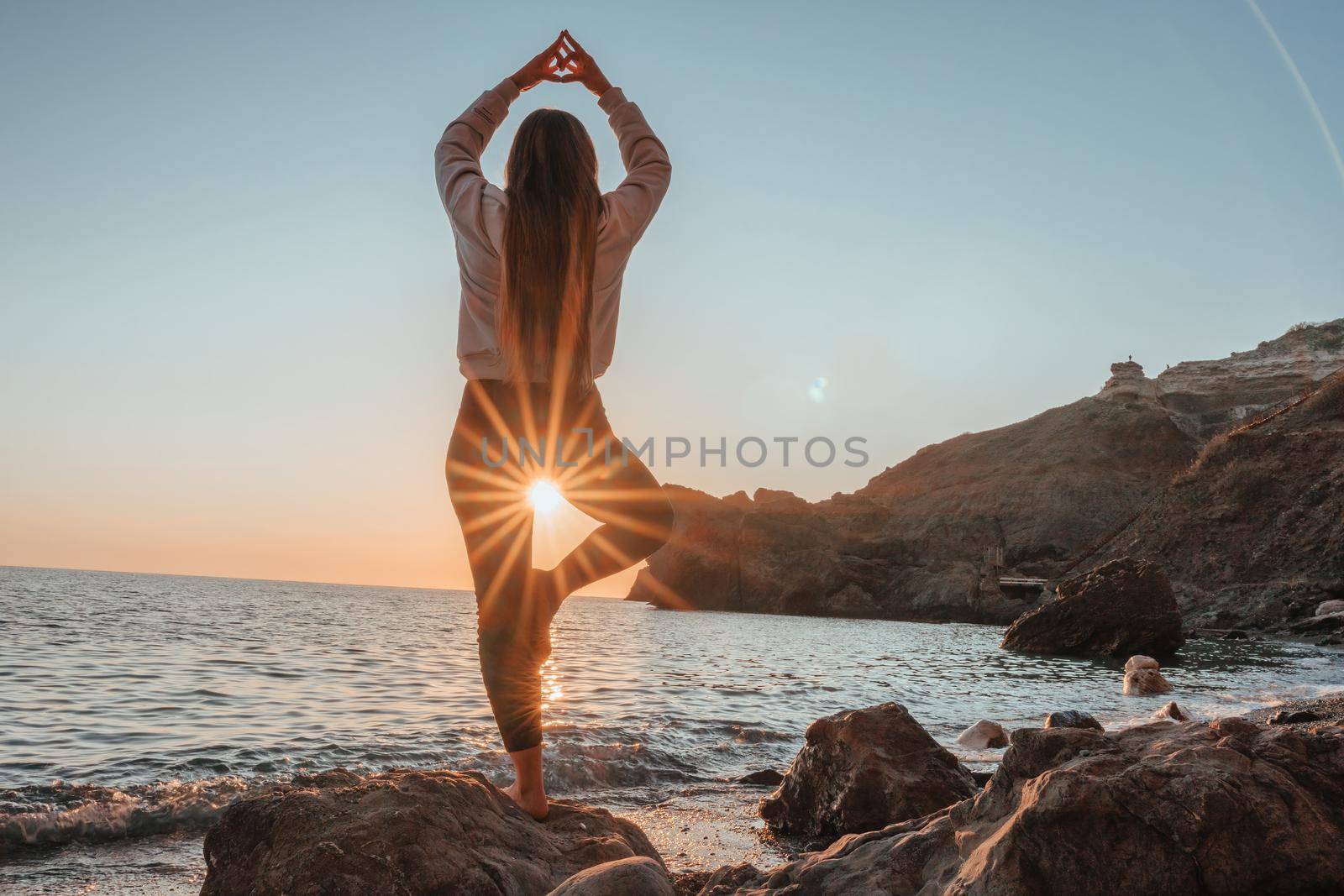 Young woman in swimsuit with long hair practicing stretching outdoors on yoga mat by the sea on a sunny day. Women's yoga fitness pilates routine. Healthy lifestyle, harmony and meditation concept.