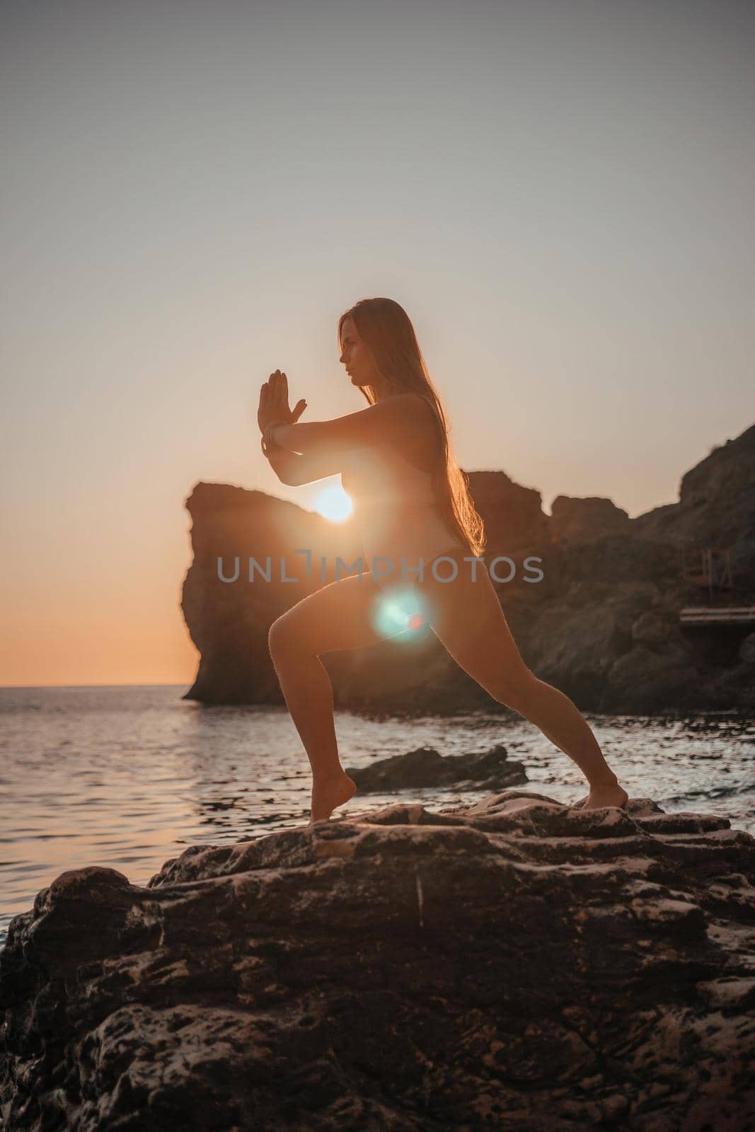 Young woman in swimsuit with long hair practicing stretching outdoors on yoga mat by the sea on a sunny day. Women's yoga fitness pilates routine. Healthy lifestyle, harmony and meditation concept.