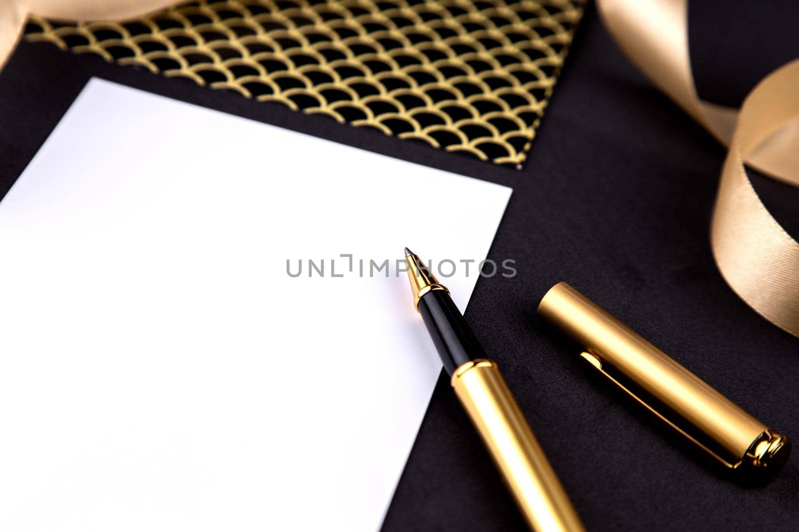 Gold pen, ribbon, paper clips and stationery on a black background with a white sheet of paper with copy space by lunarts