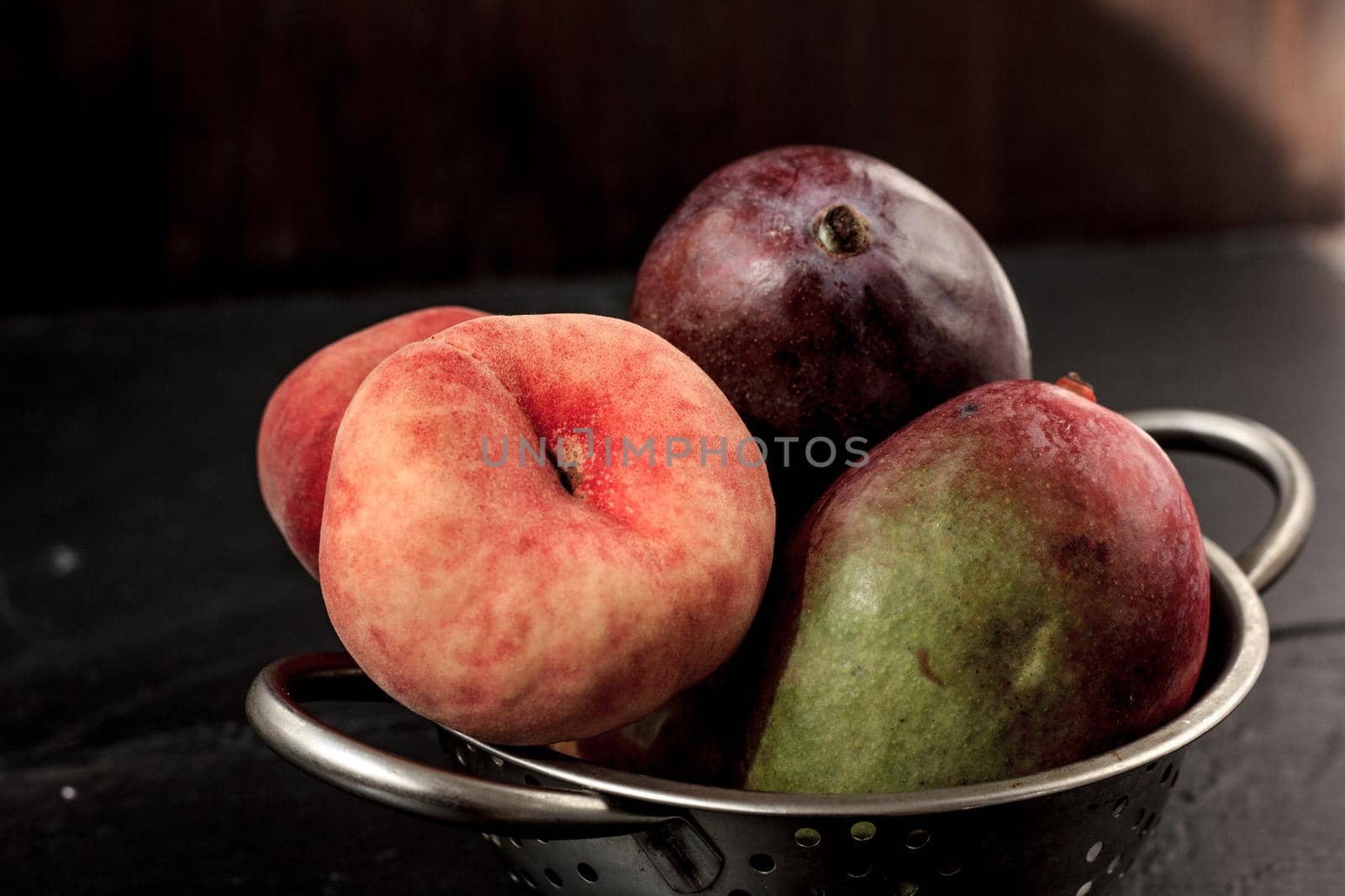 Mango and peach fruits in metal colander.