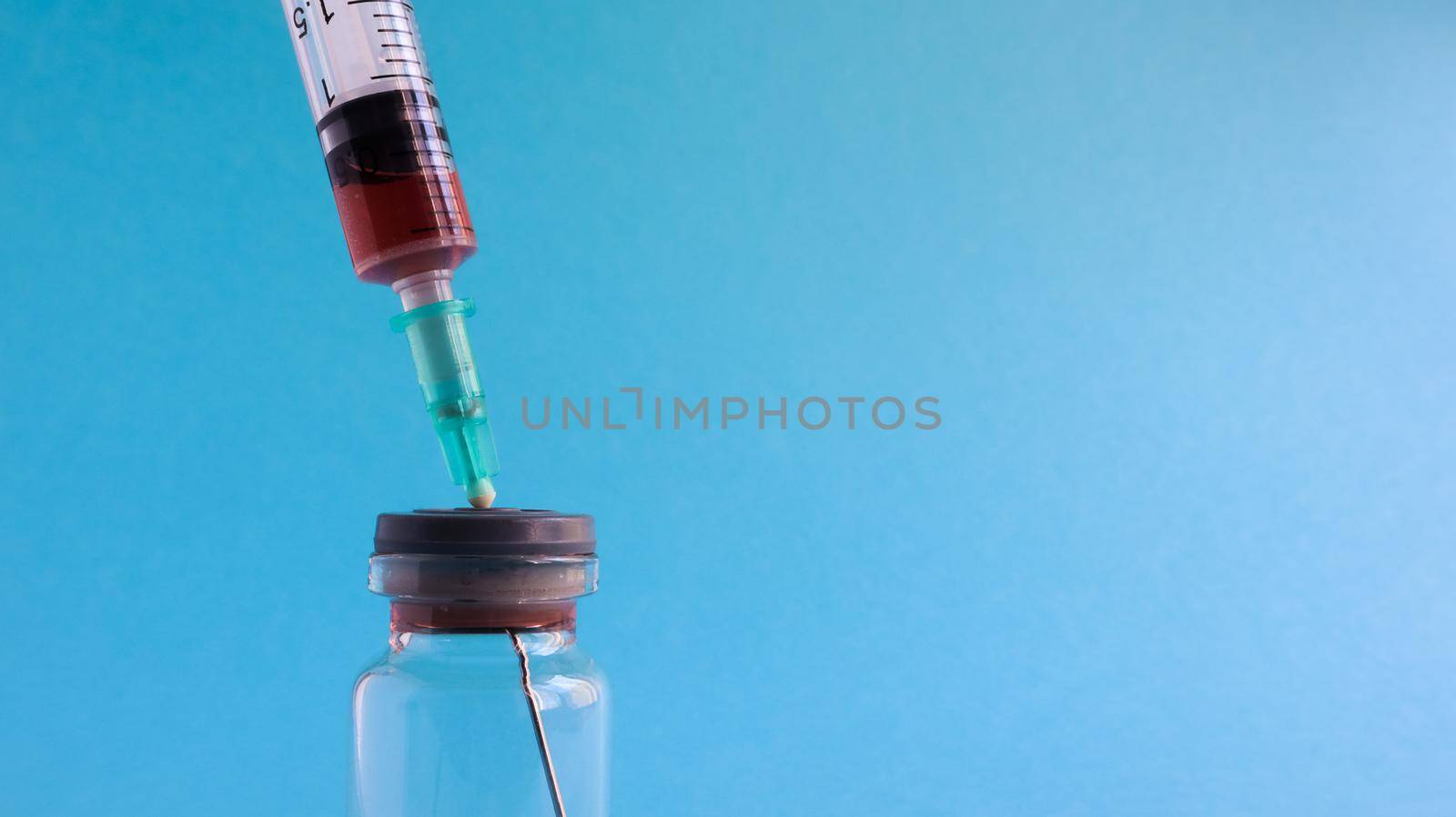 Coronavirus flu and pandemic vaccines, syringe and vial with red liquid on a blue background. medical concept, subcutaneous injection, treatment of the disease. Copy space for text or logo.