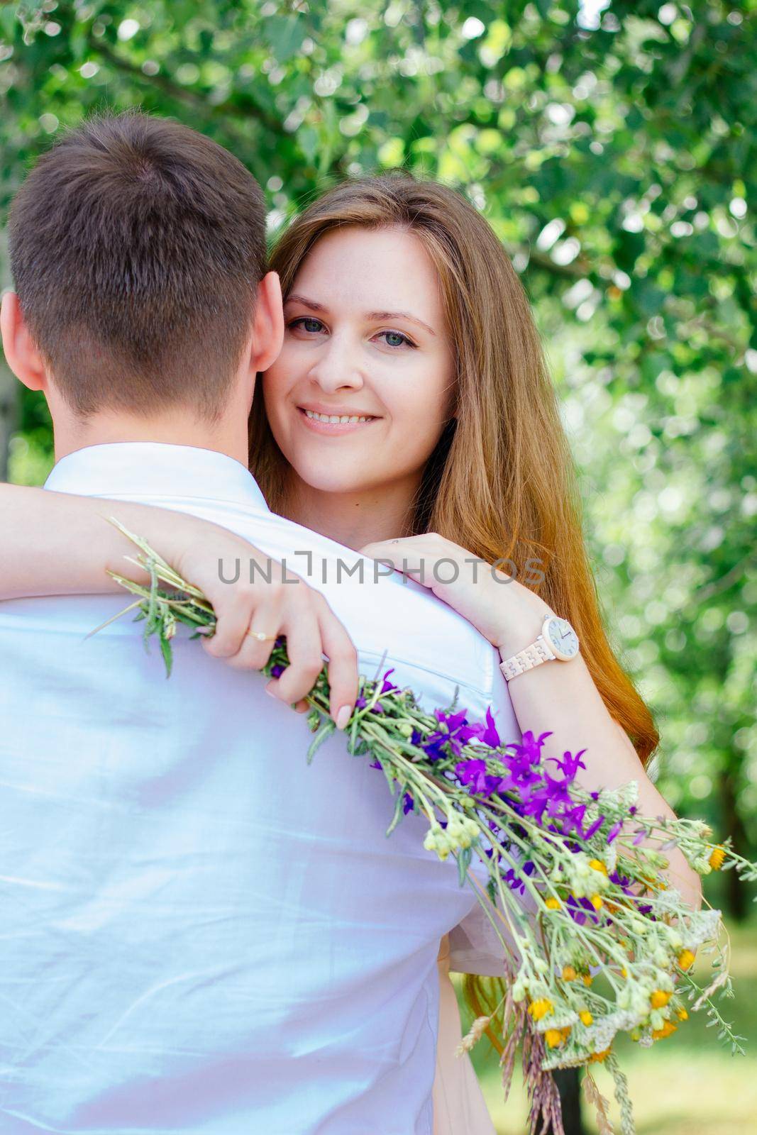 Beautiful girl huggs guy with the meadow flowers bouquet in hands