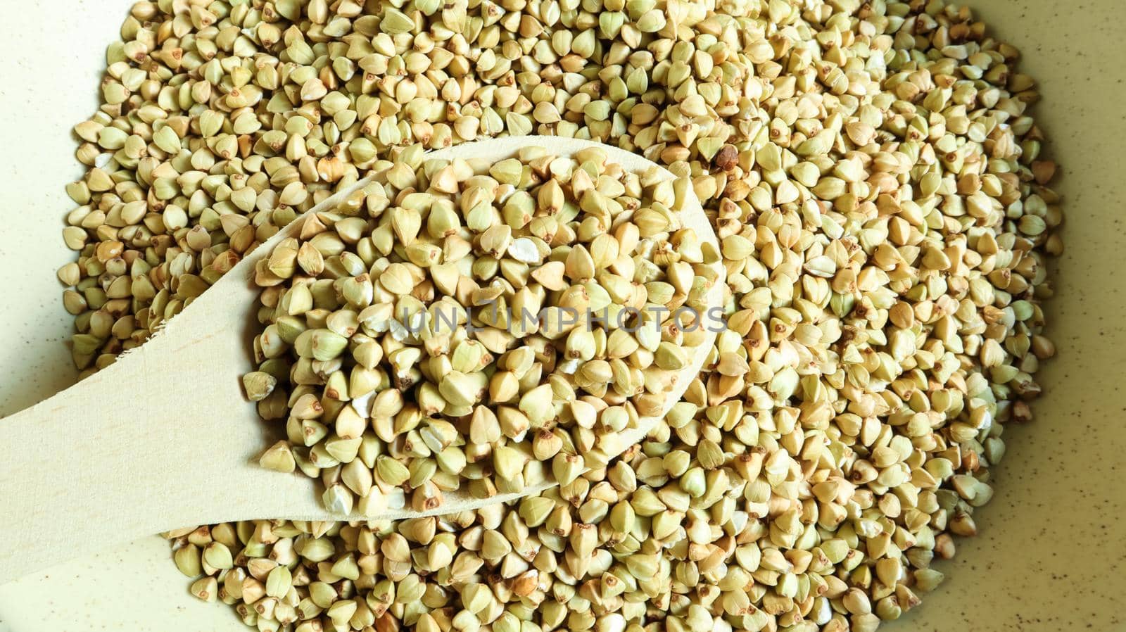 Uncooked green buckwheat in a beige plate with a wooden spoon. Great food. healthy groats. Organic raw non-fried vegetarian food. The concept of a healthy and balanced diet. Dietary foods