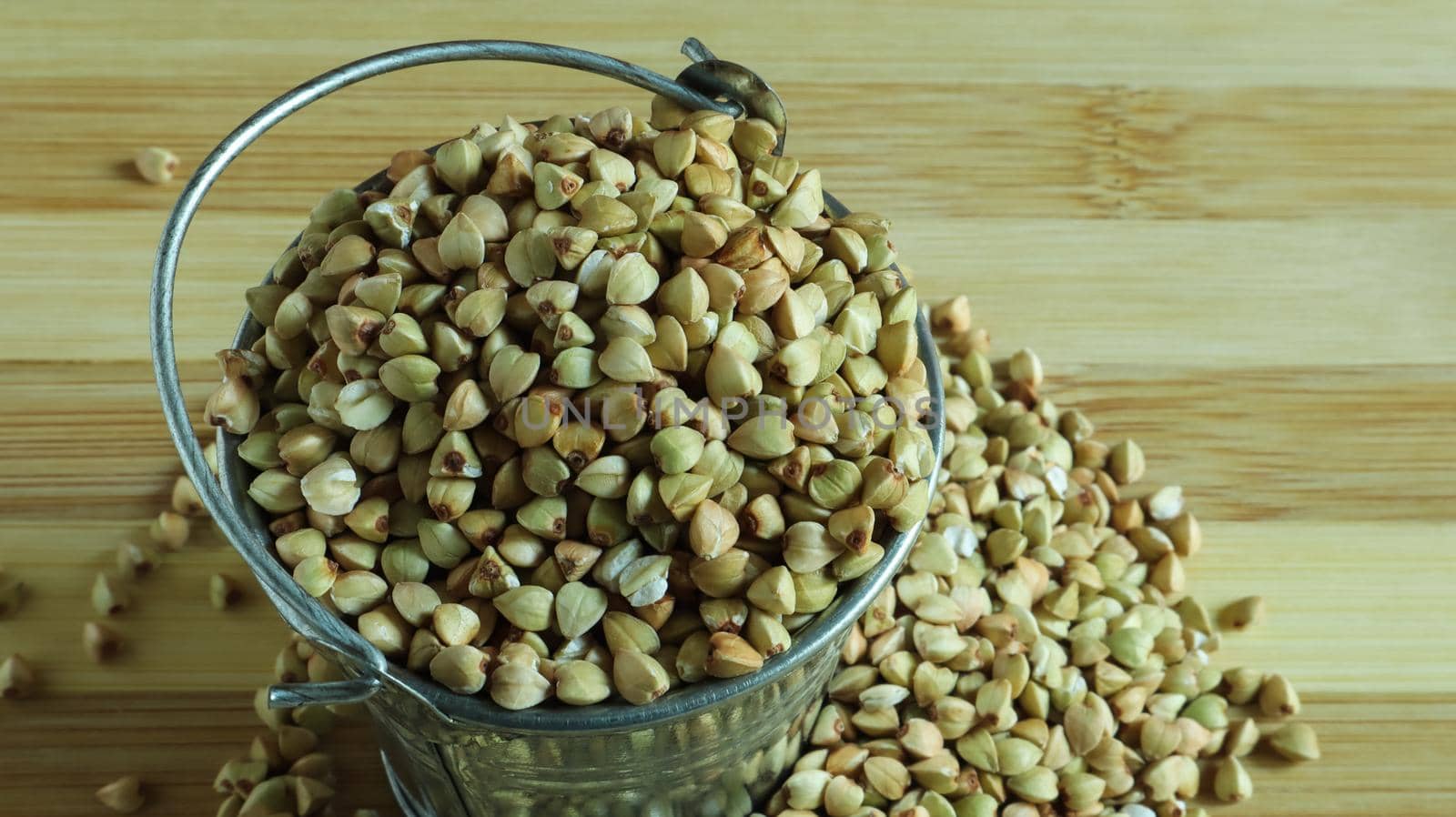 Small metal bucket with raw buckwheat on a board on a brown background. Organic vegetarian food. The concept of a healthy and balanced diet. Dietary nutrition. Copy space. Top view