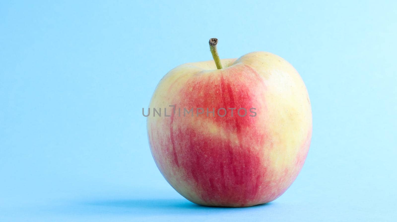 One beautiful, appetizing and fresh apple on a blue background. Healthy sweet food concept
