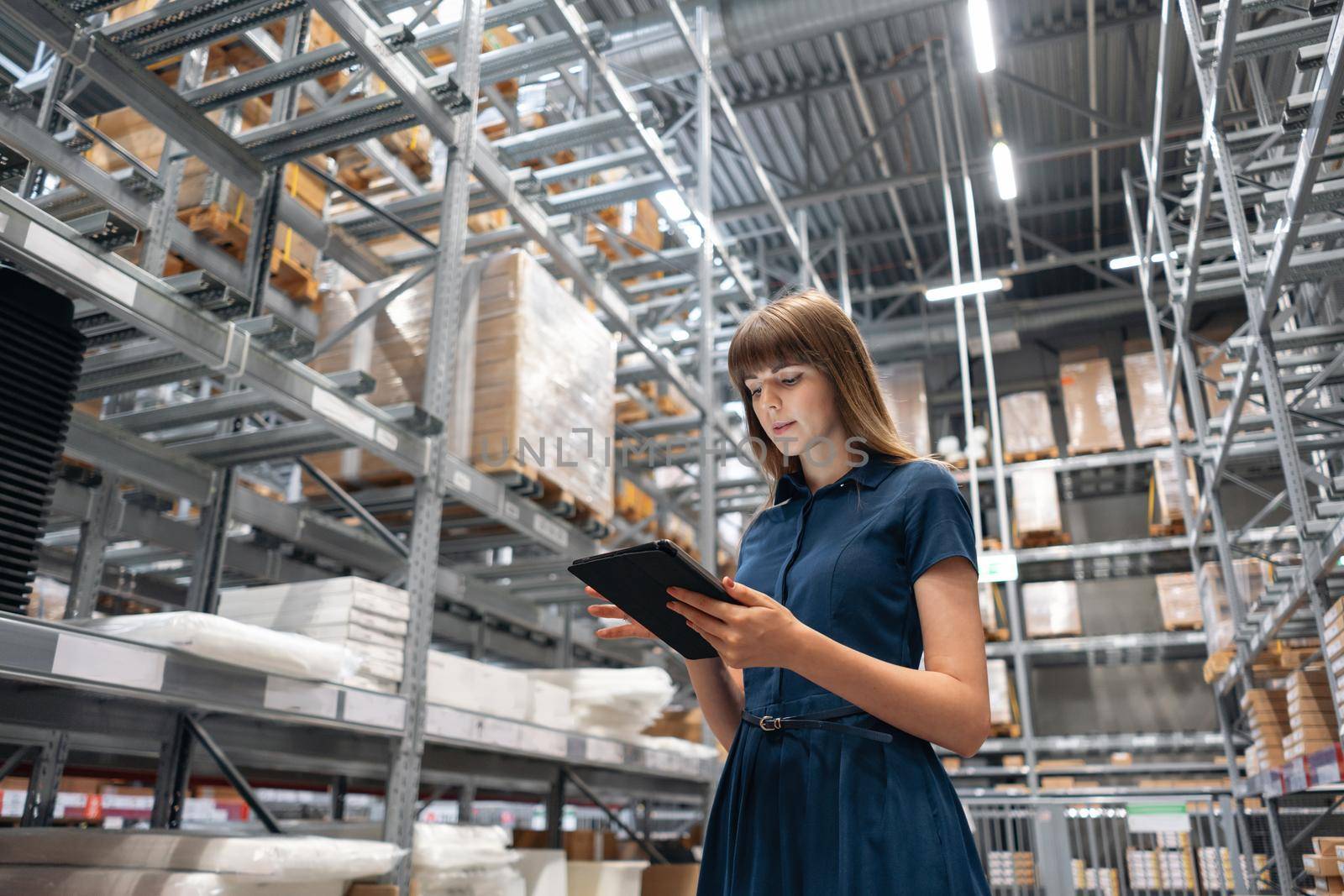 Wholesale warehouse. Beautiful young woman worker of store in shopping center. Girl looking for goods with a tablet is checking inventory levels in a warehouse. Logistics concept.