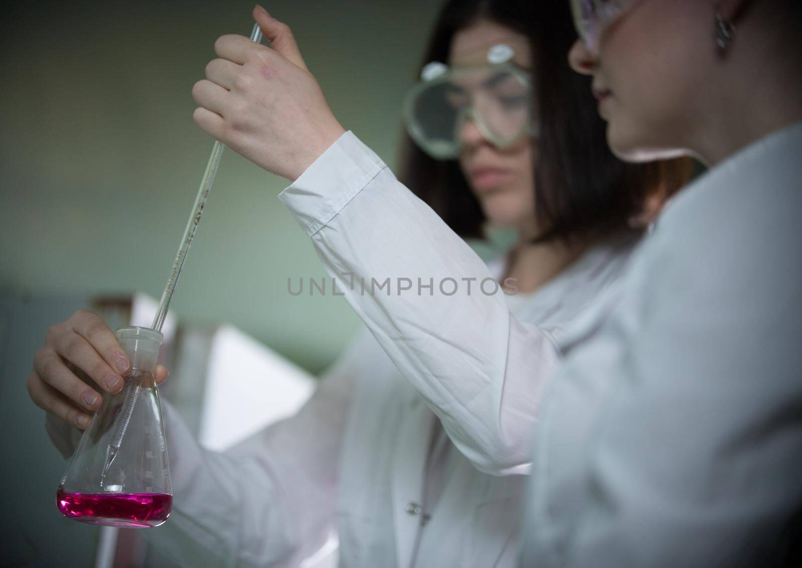 Chemical laboratory. Two young woman holding a flask with pink liquid in it. Close up