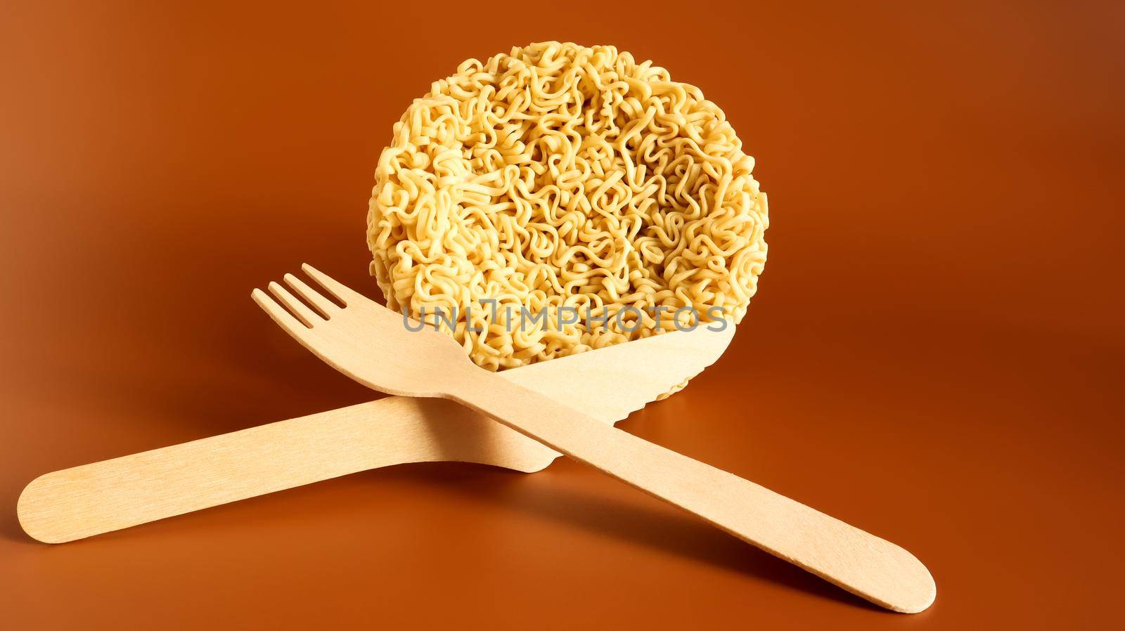 Raw instant noodles in the shape of a circle with a wooden disposable fork. pasta, for the preparation of which it is enough to pour boiling water and wait a few minutes. spaghetti. Copy space.
