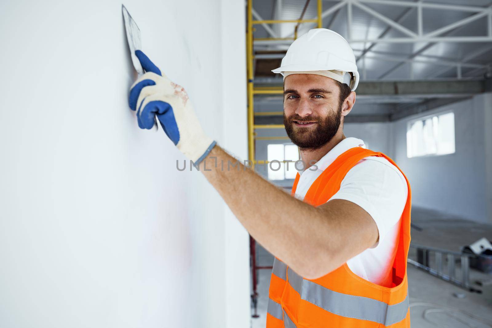 Plasterer in workwear smoothing wall surface of building indoors, close up