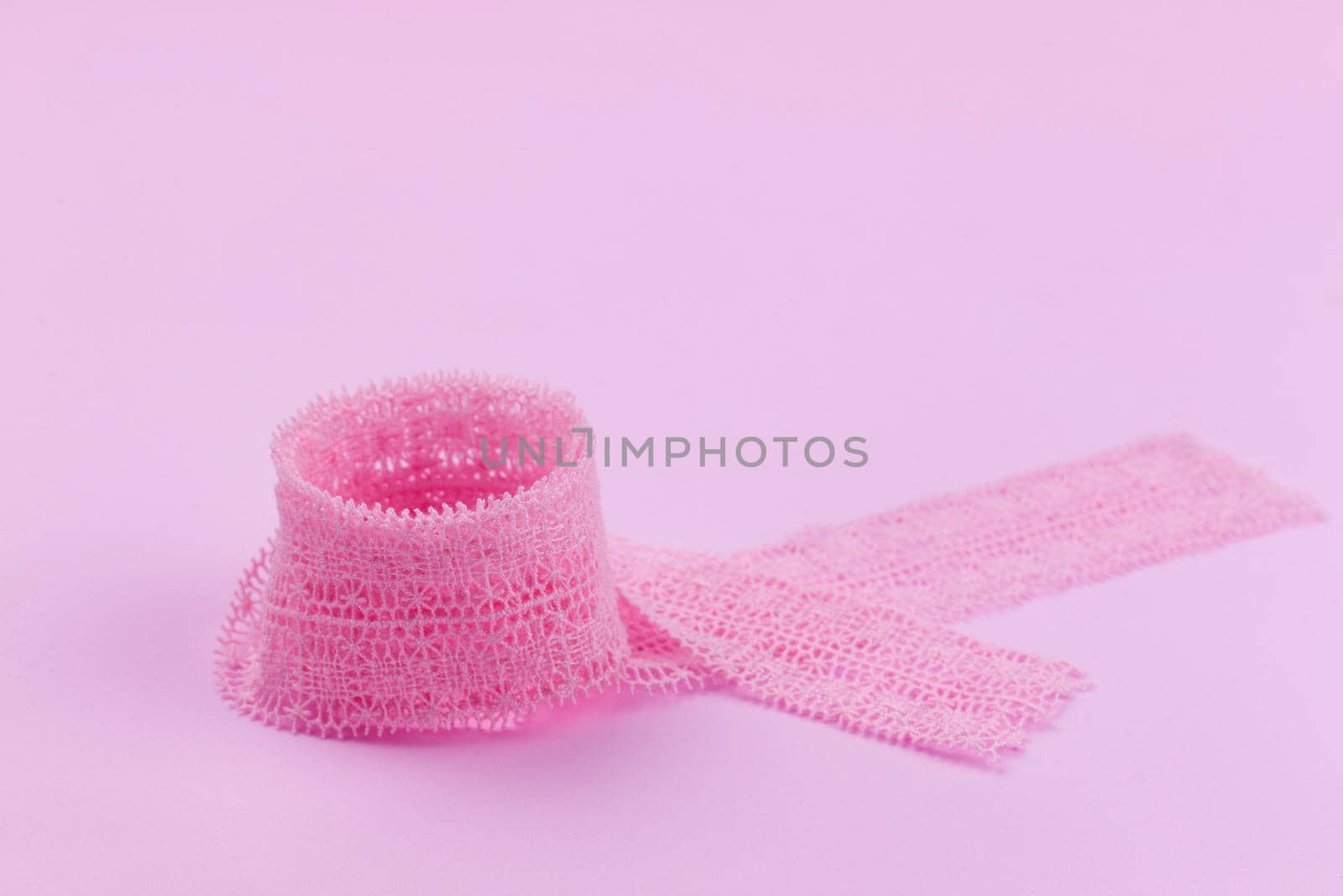 Lace ribbon neatly twisted into a ring on a pink background. Romantic background.