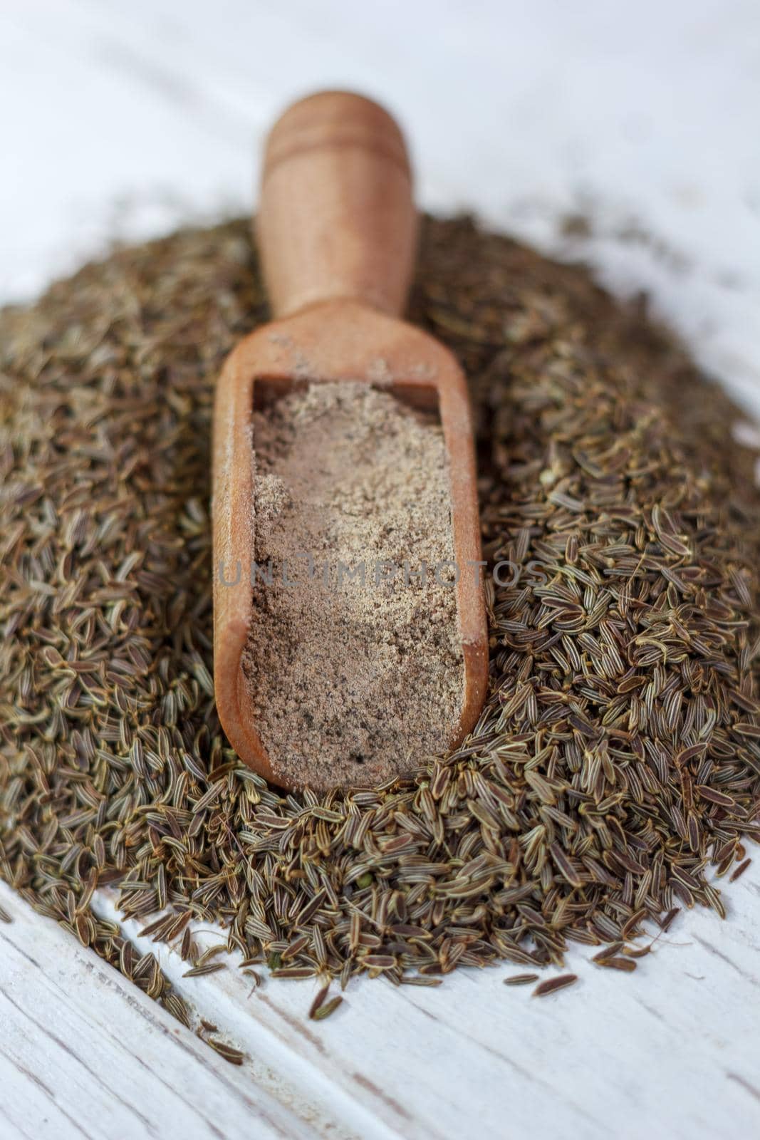 Grounded cumin seeds in a wooden spoon over the seeds