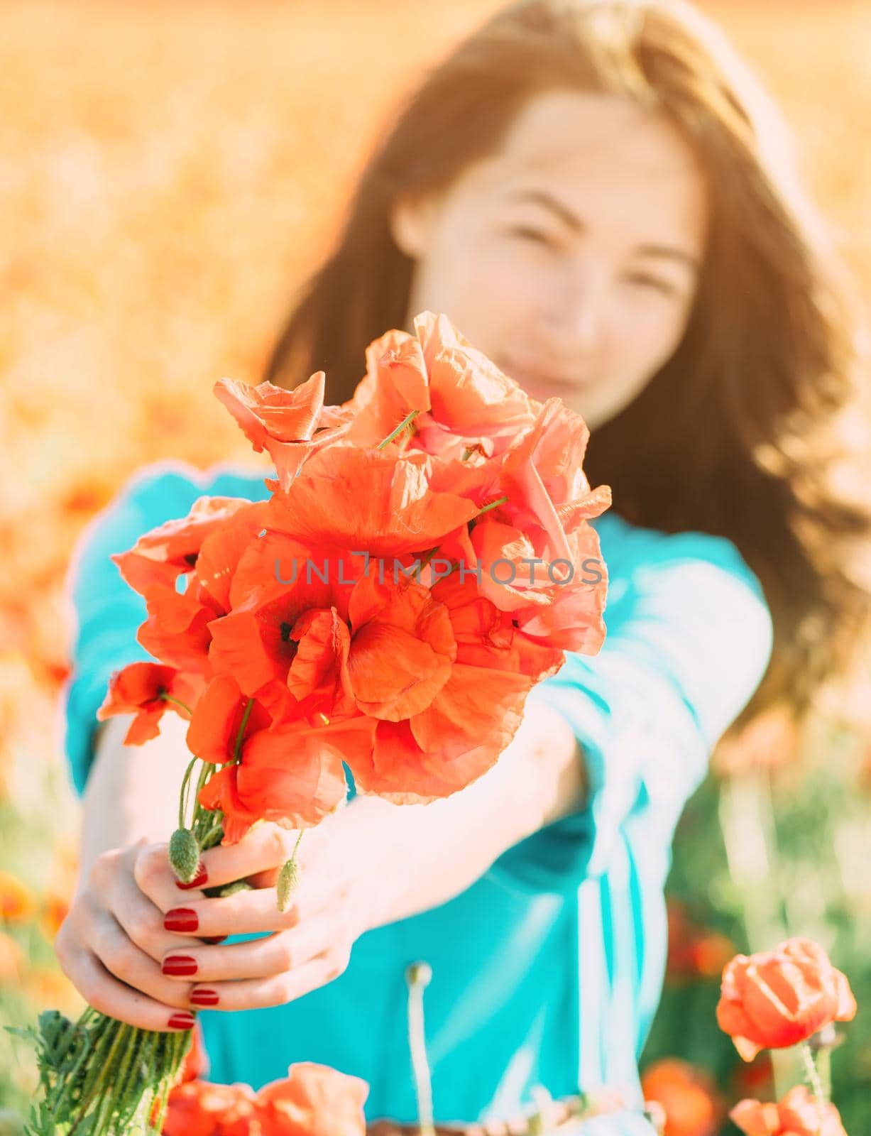 Beautiful brunette young woman giving a bouquet of poppies outdoor, focus on flowers.