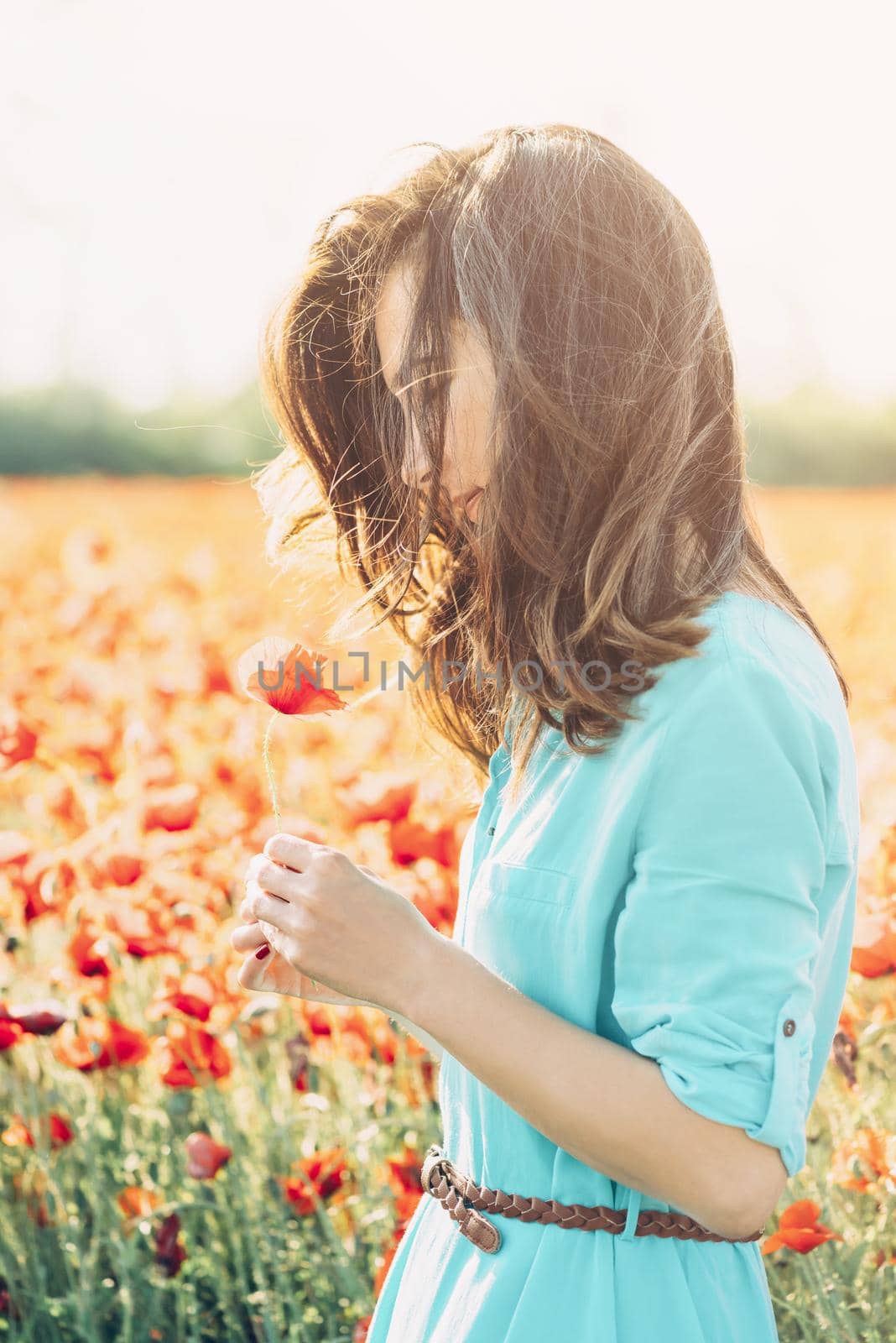 Smiling beautiful young woman standing with poppy in flower meadow.