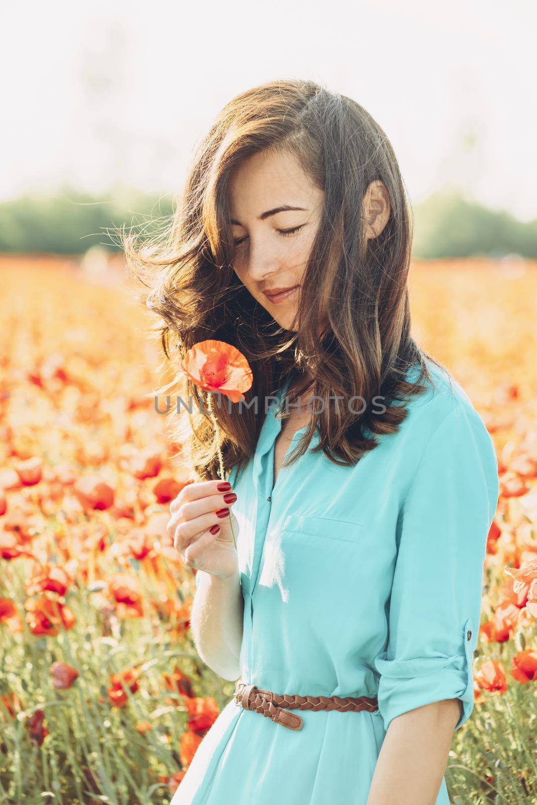 Happy beautiful young woman standing with poppy in flower field.