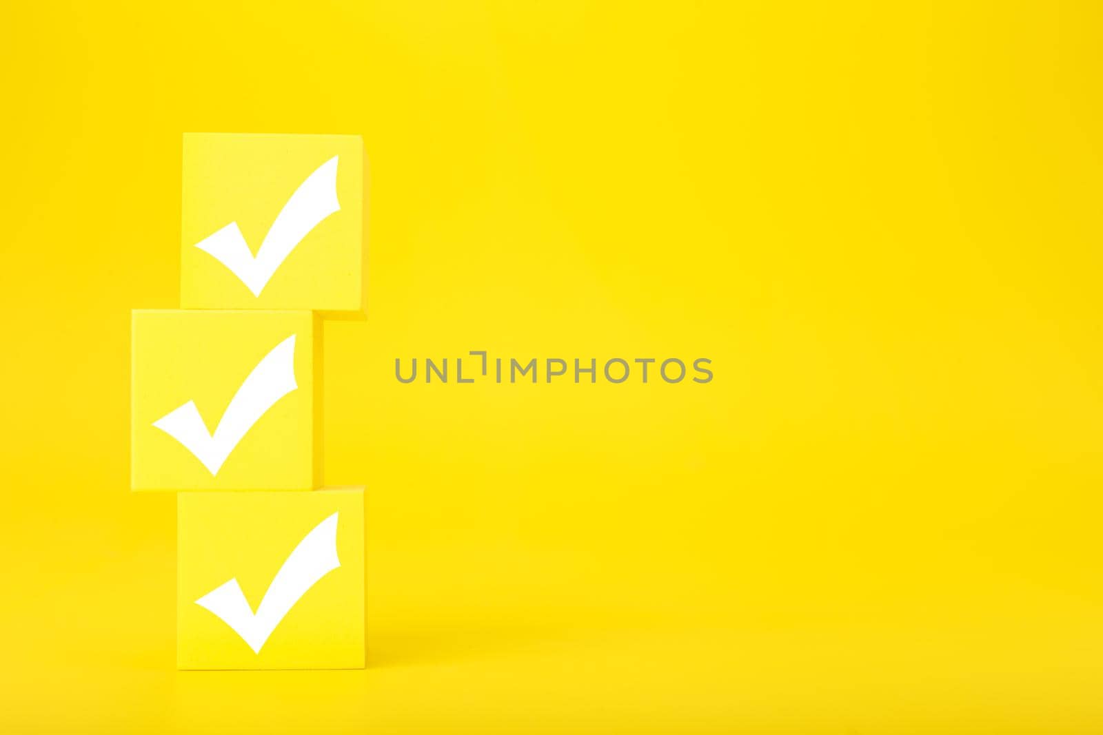 Three white checkmarks on yellow toy cubes against bright yellow background with copy space by Senorina_Irina