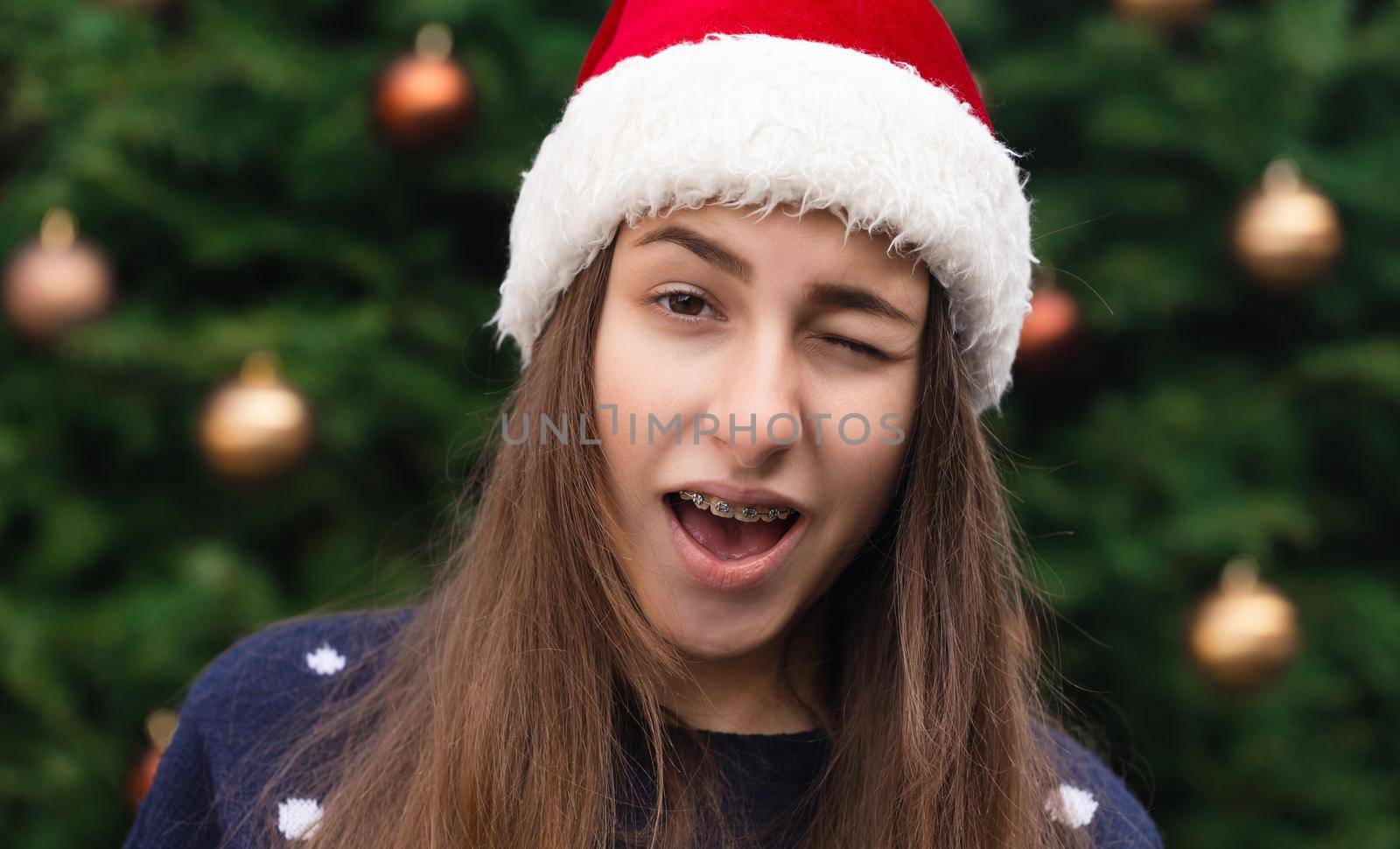 Everything will be fine for christmas. Close up Portrait of woman wearing a santa claus hat with emotion. Against the background of a Christmas tree.