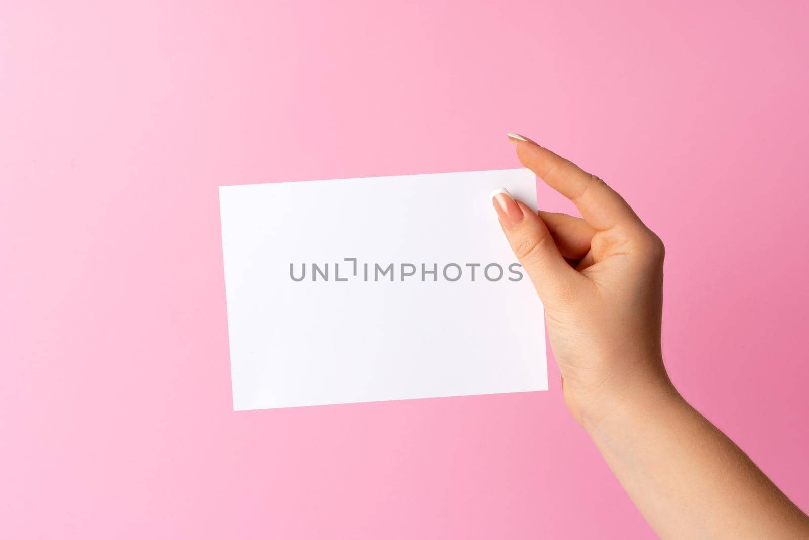 Woman hand showing blank business card on pink background. Close up.