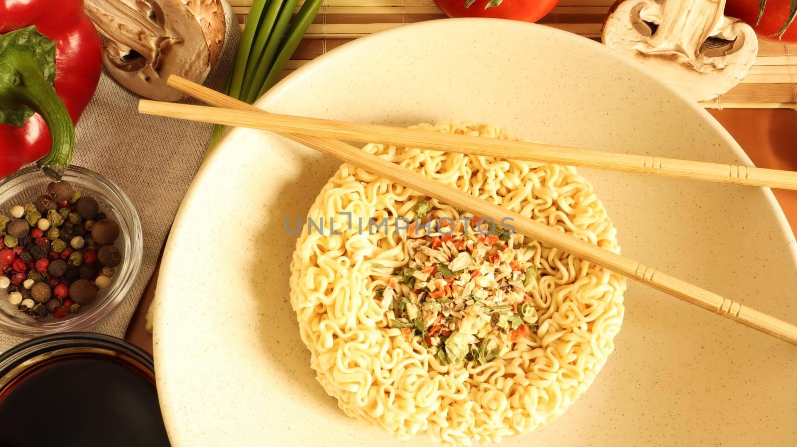 Instant noodles with king mushrooms, seasonings, soy sauce, peppers, green onions, tomatoes. Vegetable fast vegetarian soup. The process of cooking Asian food on the table. Vermicelli, spaghetti.