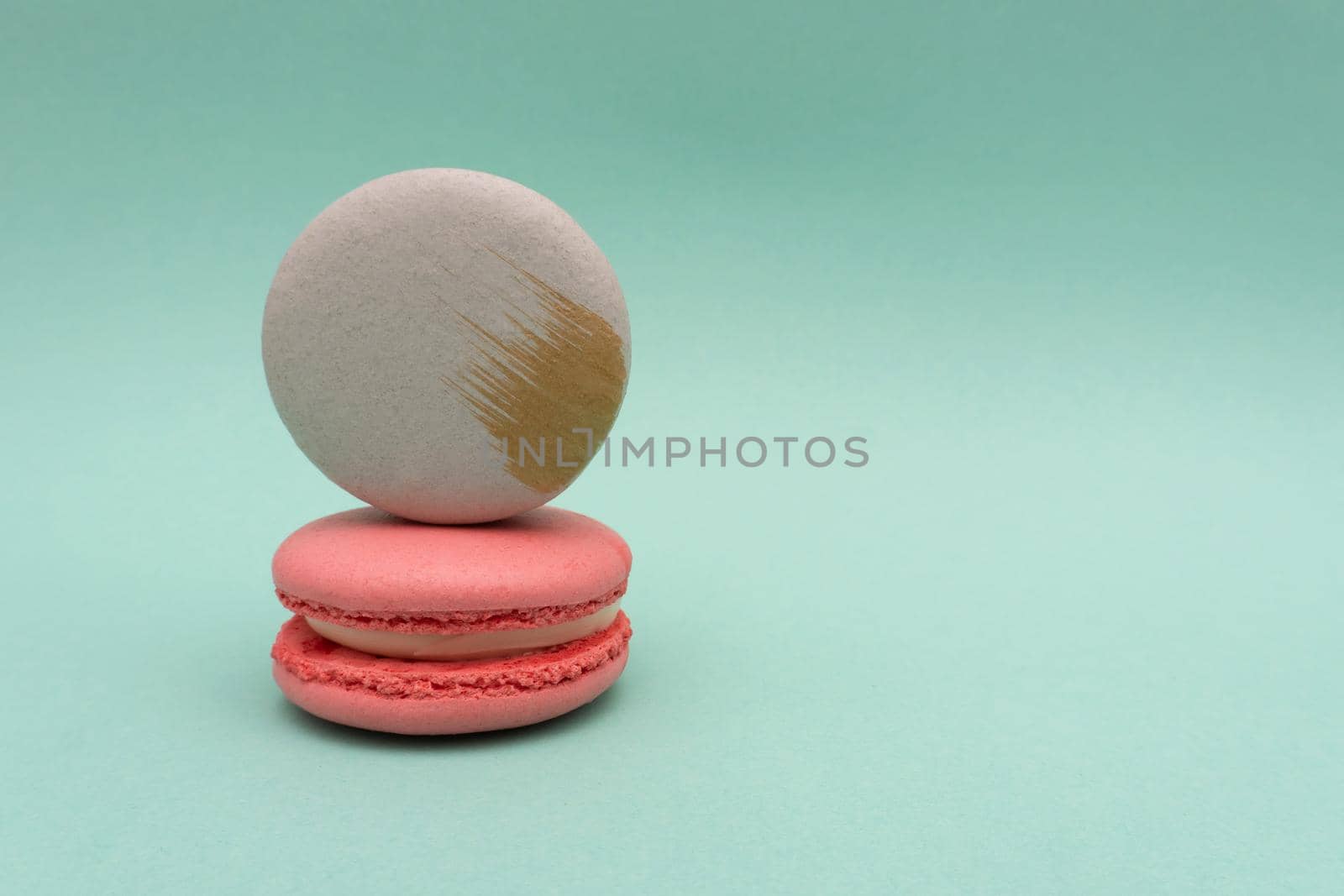 Grey grapefruit macaron stand on pink strawberry macaroon on mint or turquoise background, copy space, almond cookies, pastel colors