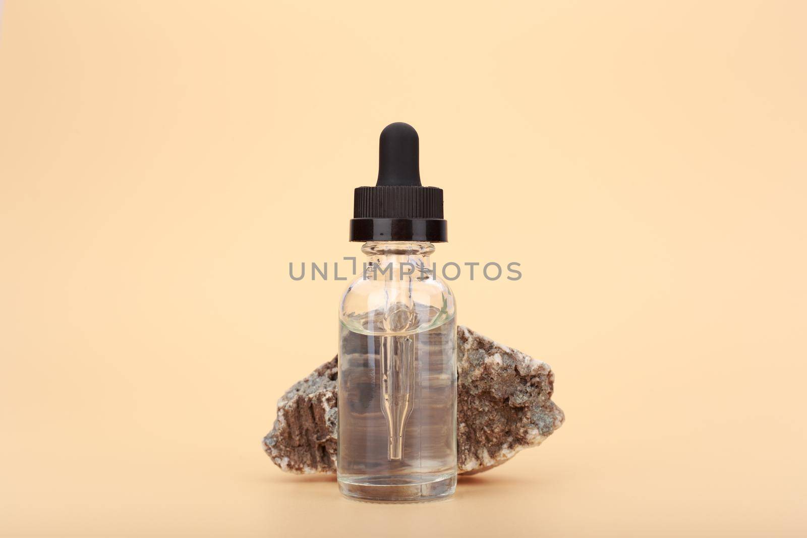 Transparent skin serum bottle close up next to natural stone against bright beige background with copy space by Senorina_Irina