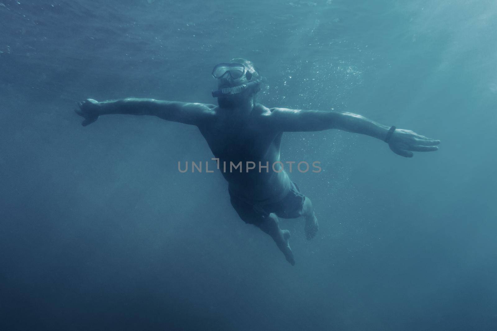 Happy active man in mask with snorkel swimming underwater on vacations.