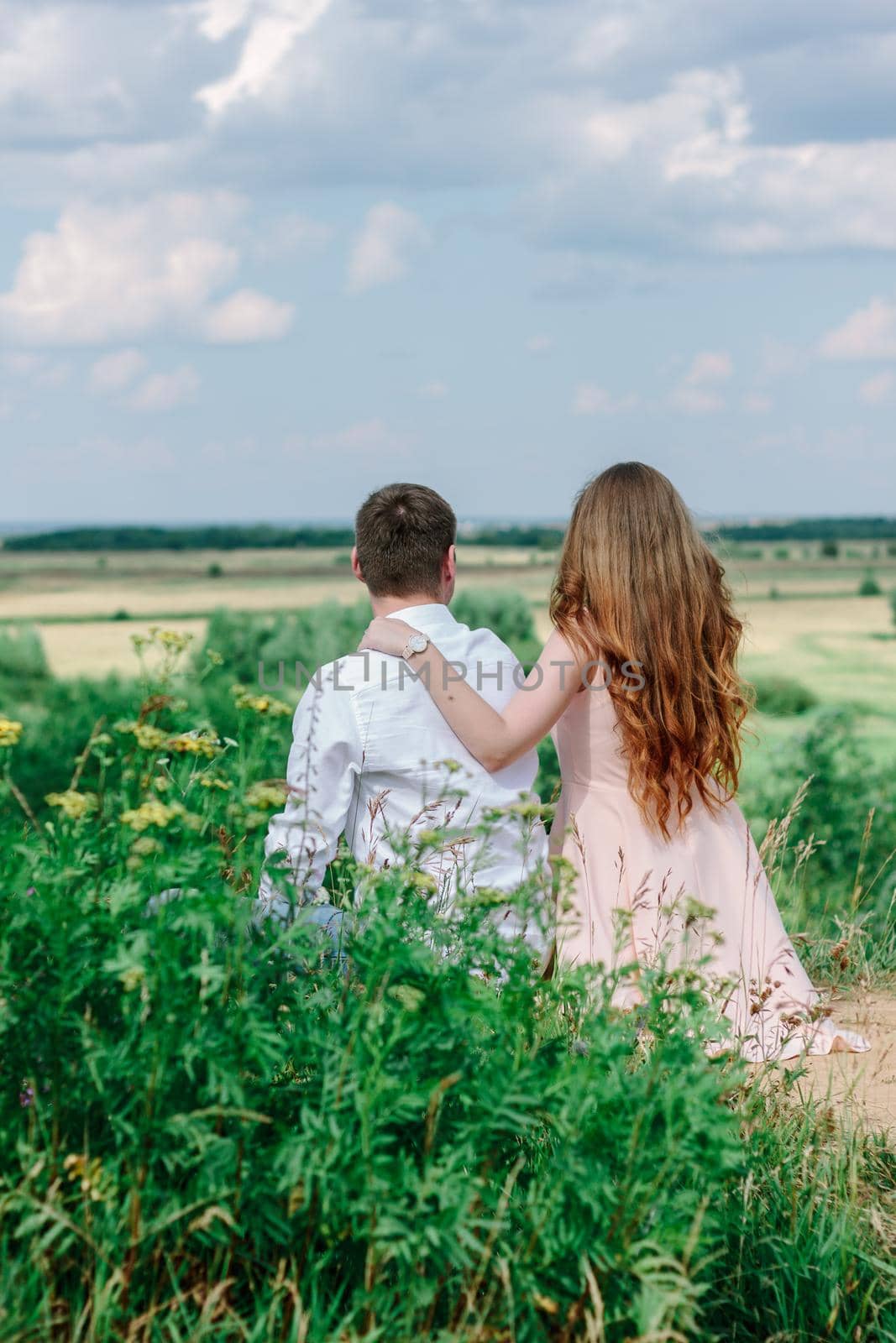 Back view of young couple sitting at the hill and looking to the valley