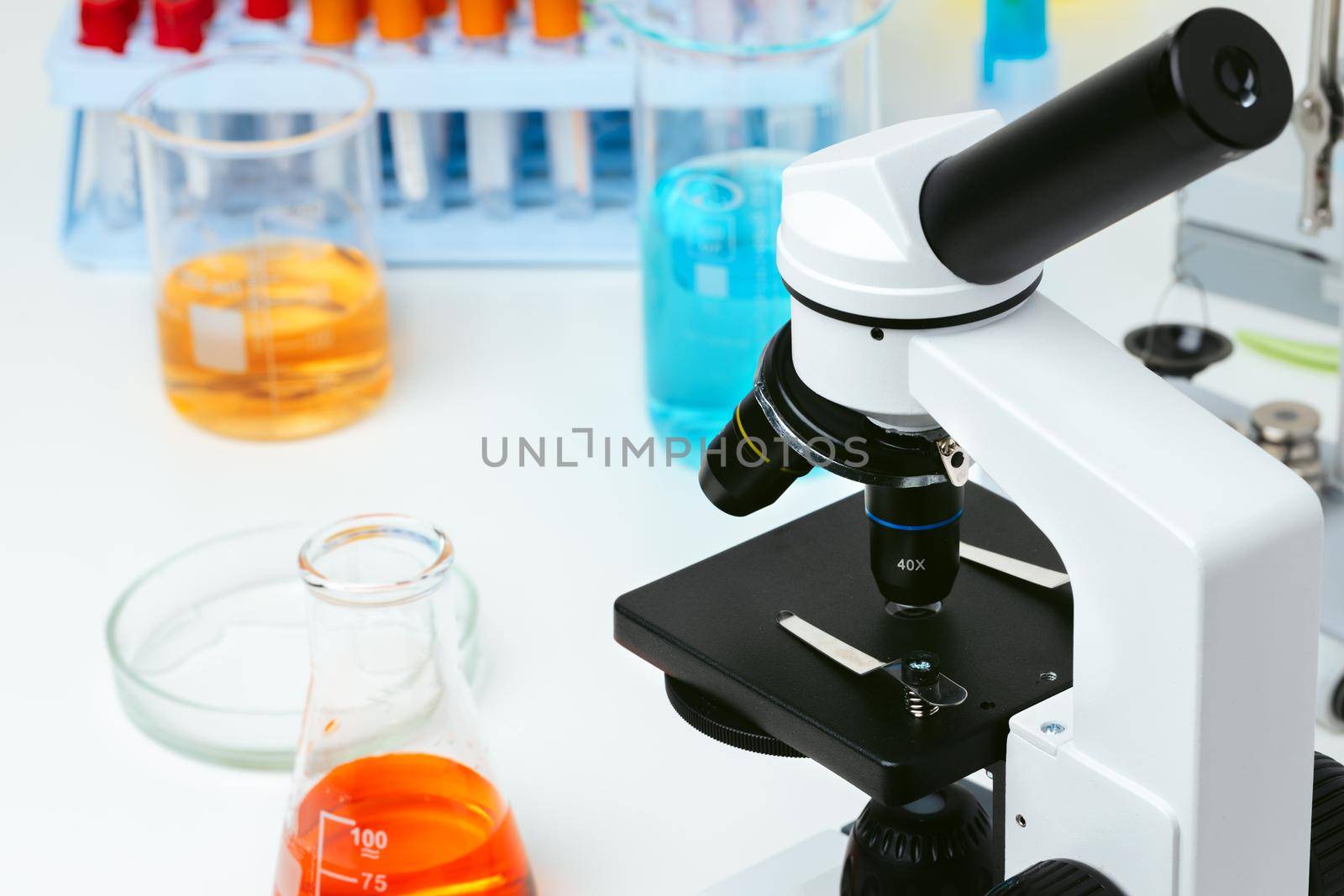 Microscope and colored test tubes on table in laboratory, close up