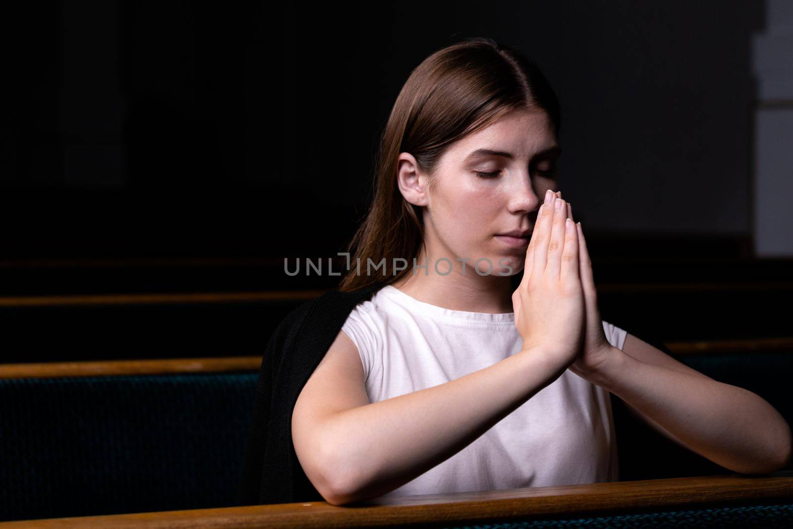 A Christian girl in white shirt is sitting and praying with humble heart in the church.