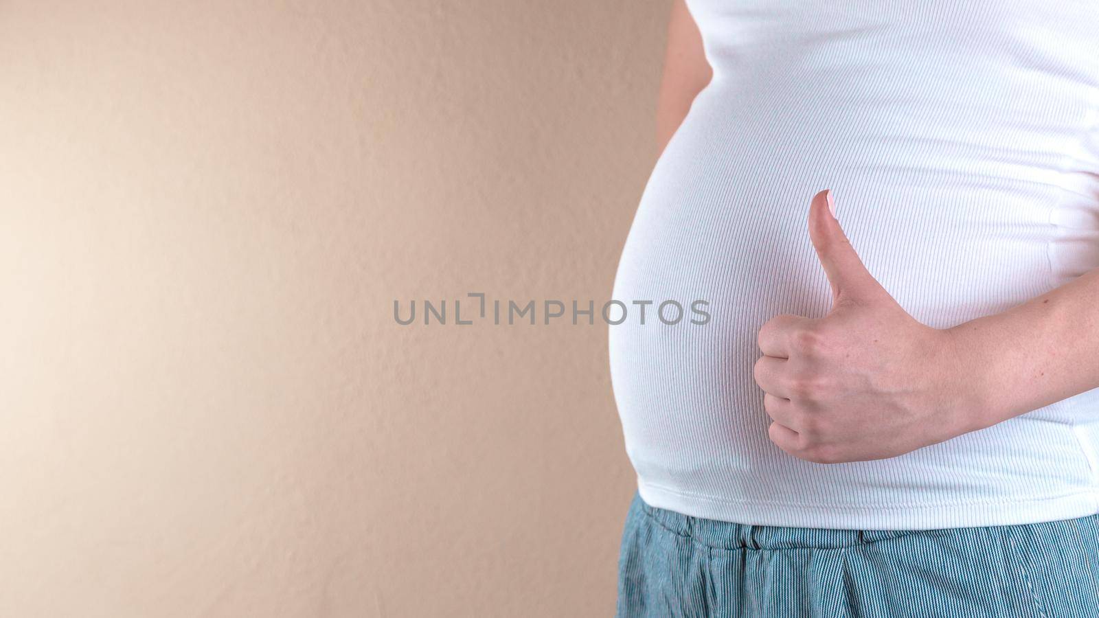 A close-up view of the belly of a pregnant woman in a white T-shirt that shows a like sign. Copy space for text by lunarts