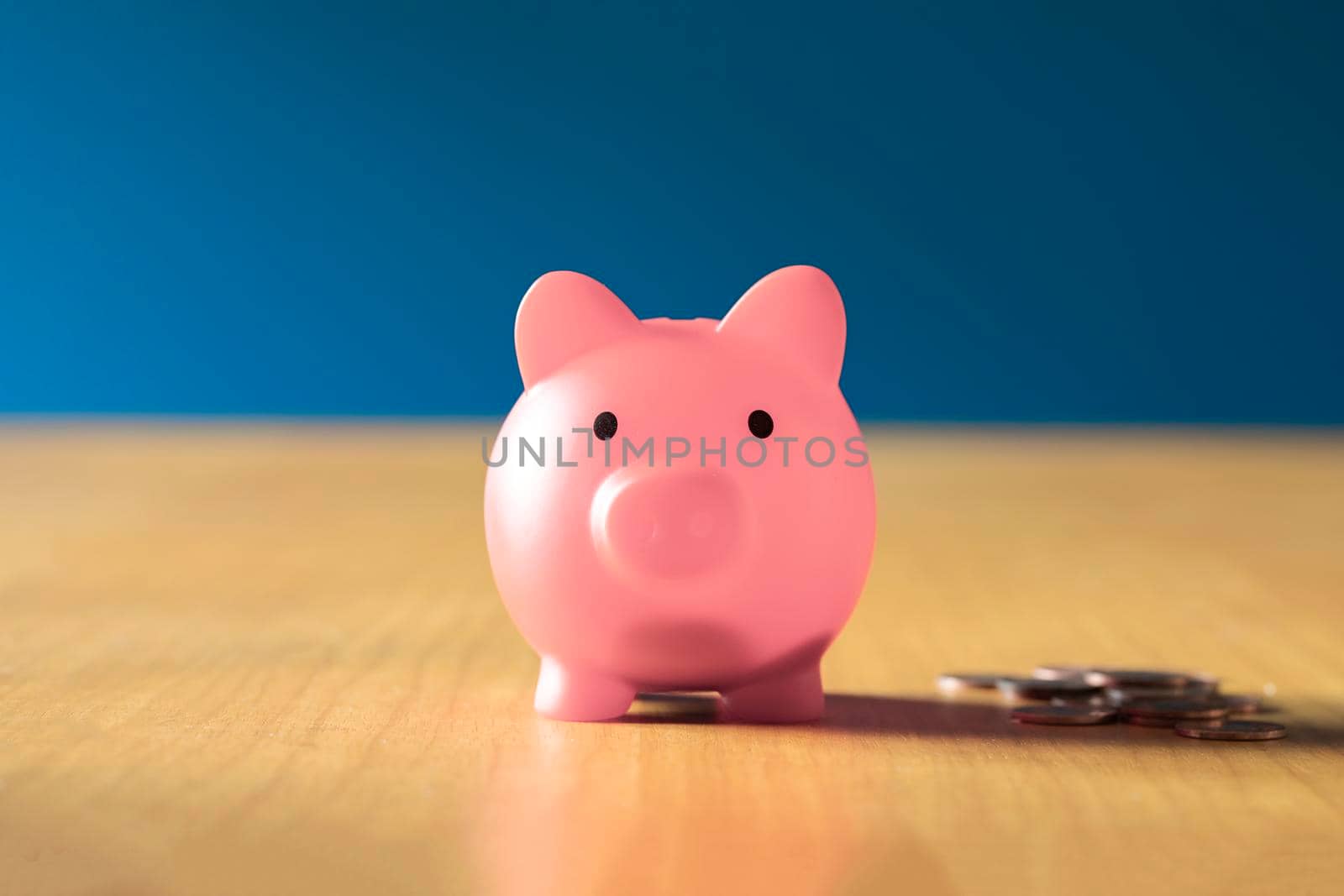 Pink piggy bank on wooden office desk at home with pile of coins, savings,investment business and financial concept close up