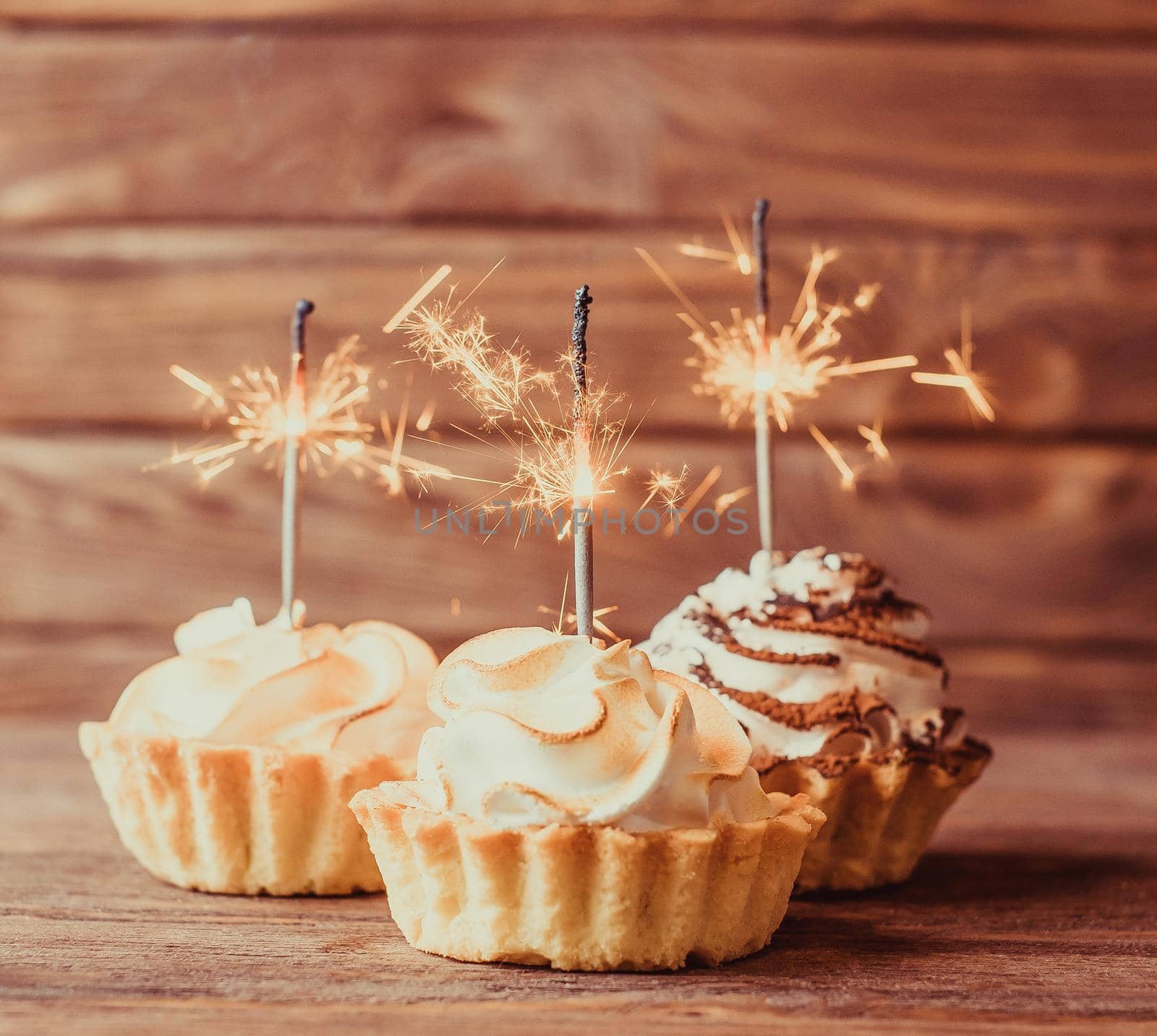 Three holiday cupcakes with sparklers on a wooden background.