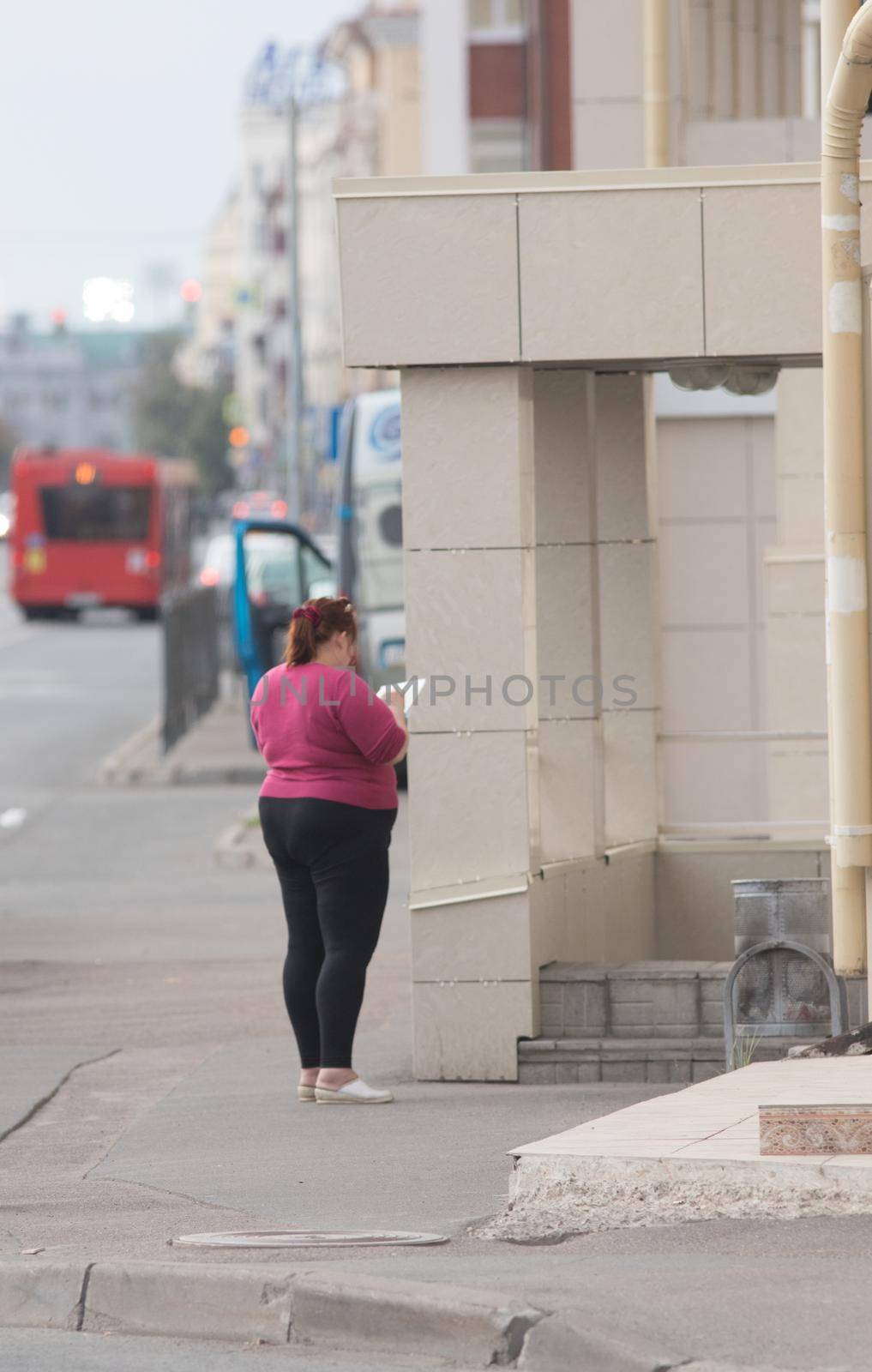 Plus-size young woman stands back to the camera and writes in a notebook on the street by Studia72