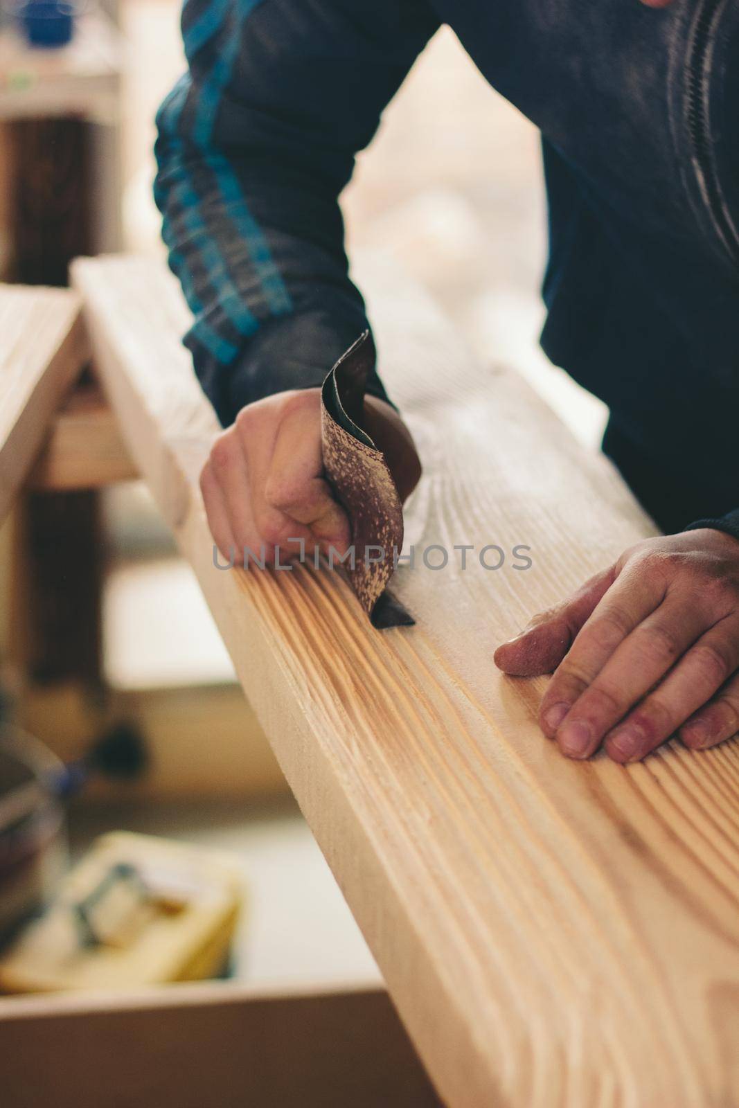 hands with the sandpaper treat the wooden plank. Great photo for your needs.
