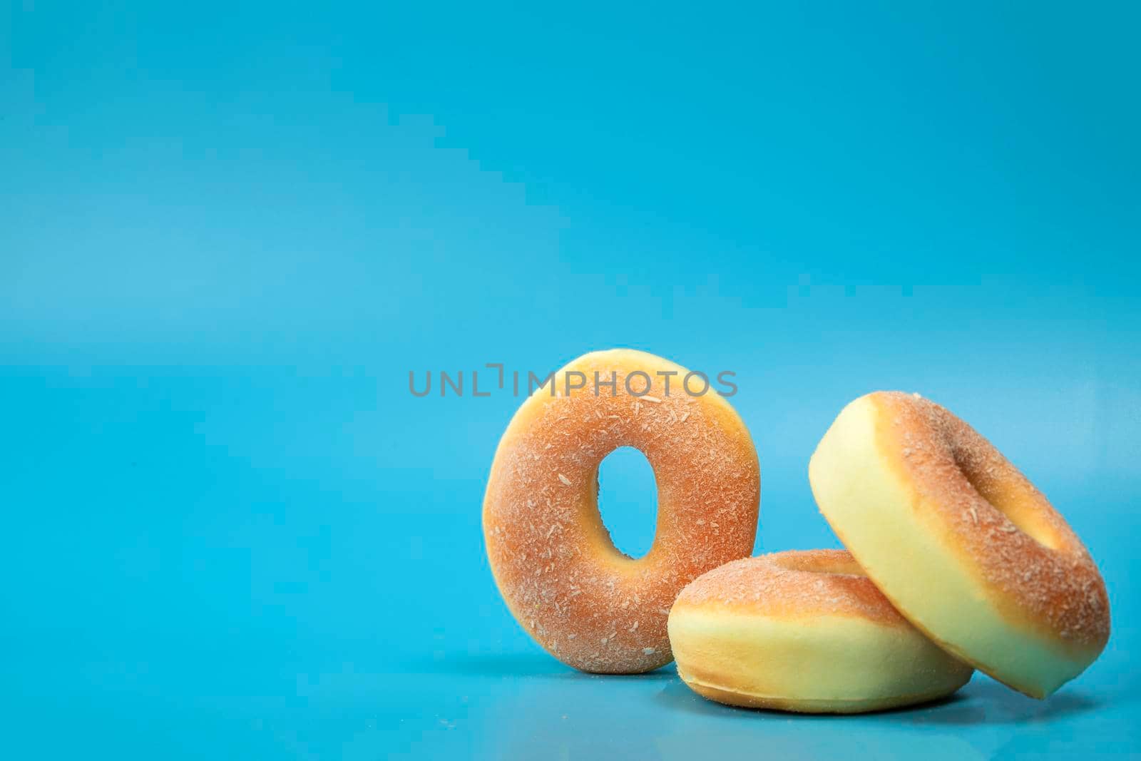 Pile with three simple donuts with sugar isolated on blue background with copyspace, fast food,sugar concept space for text
