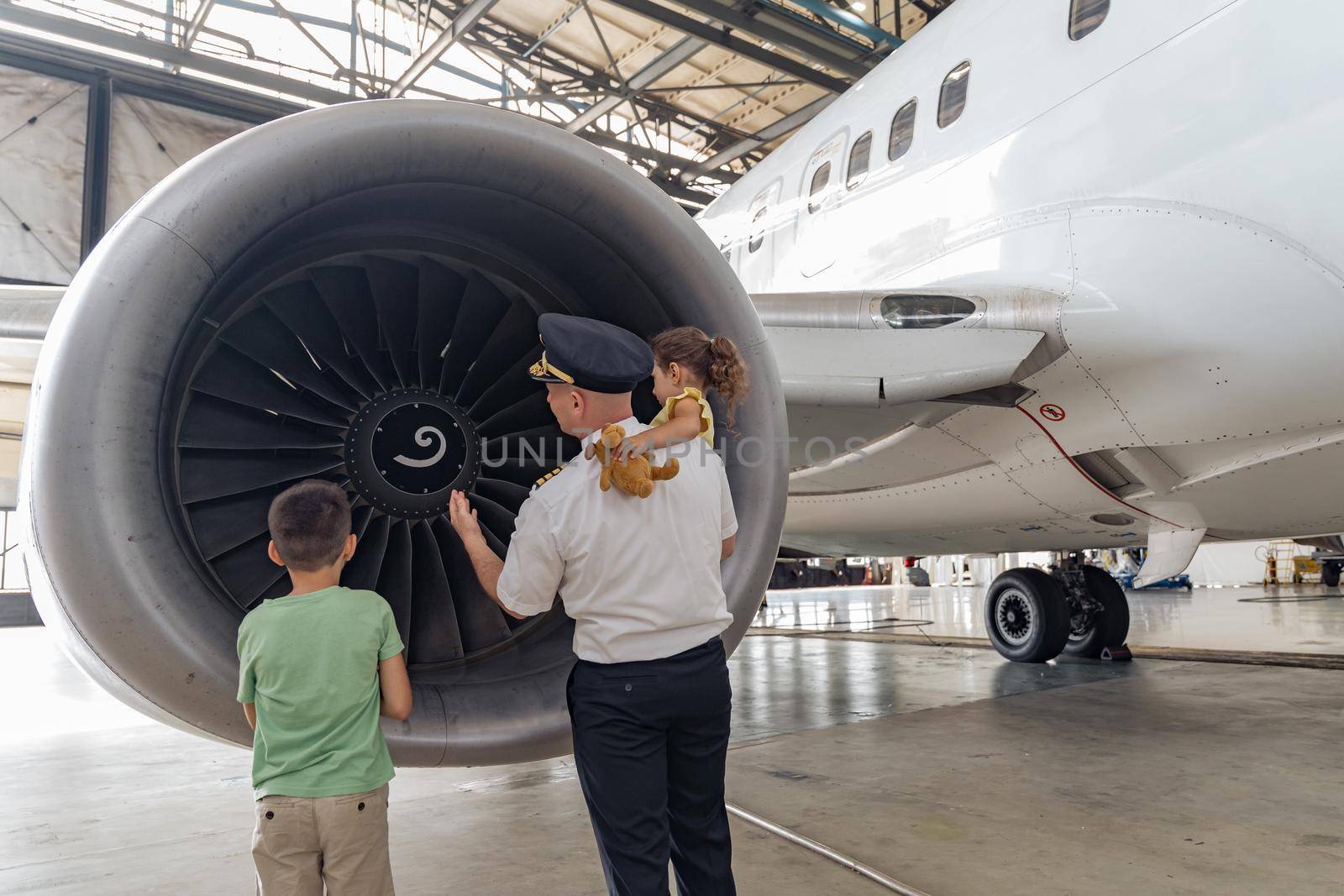 Pilot giving a tour to children near a large white plane in a hangar