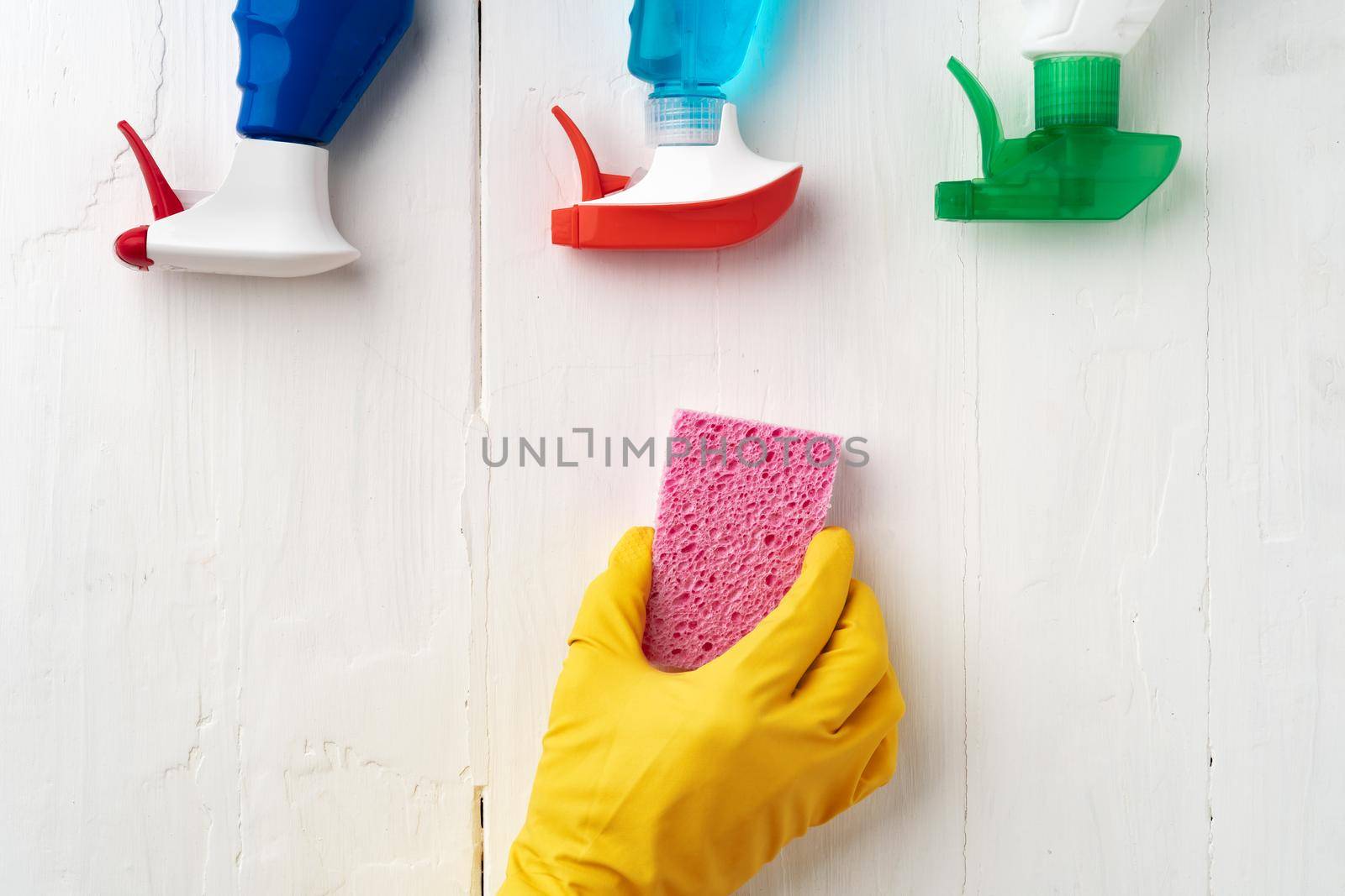 Hand in glove with cleaning supplies above white wooden background, top view