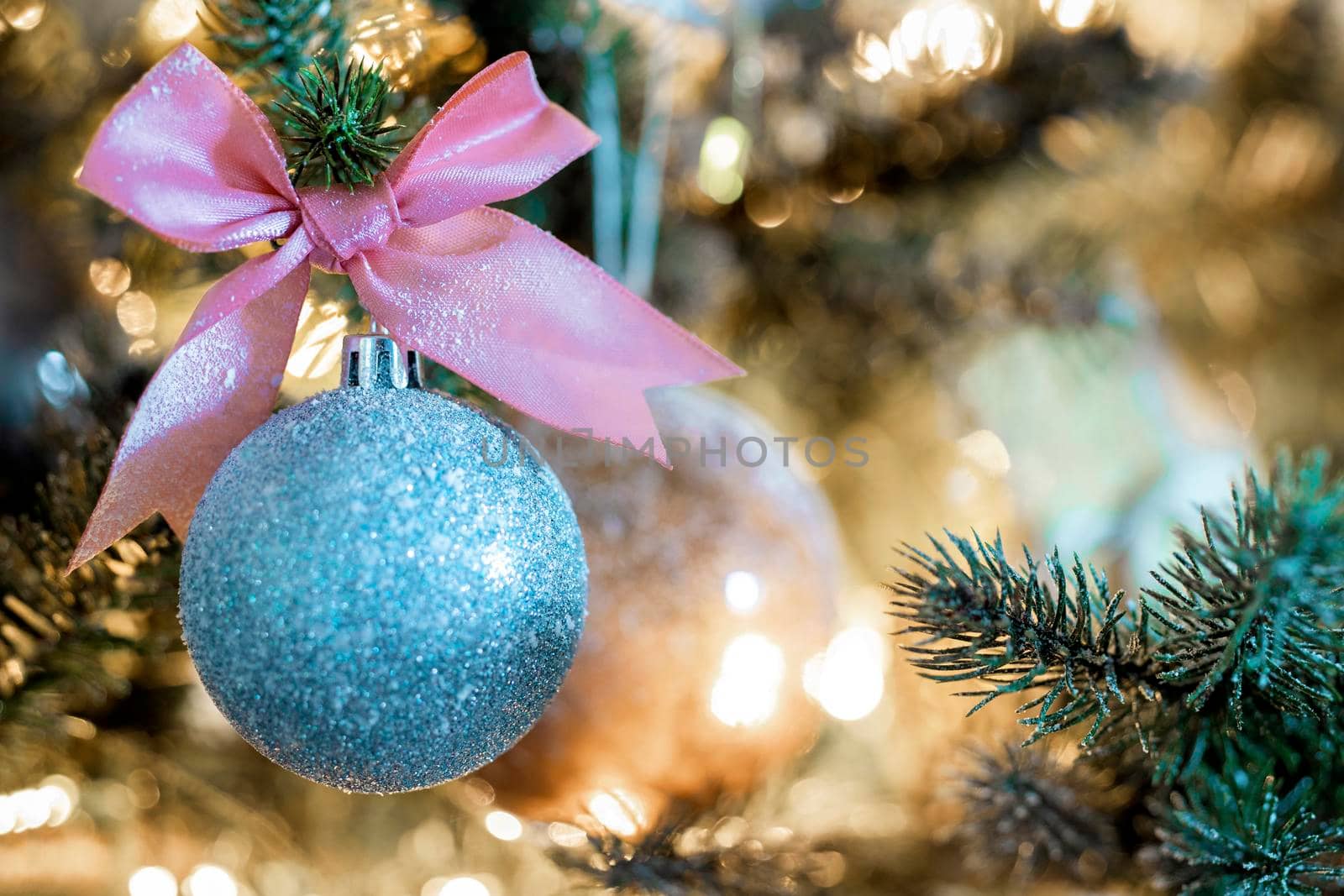 Sparkling Christmas bauble with pink bow hanging in decorated tree, copy space and bokeh light background, Holiday concept space for text