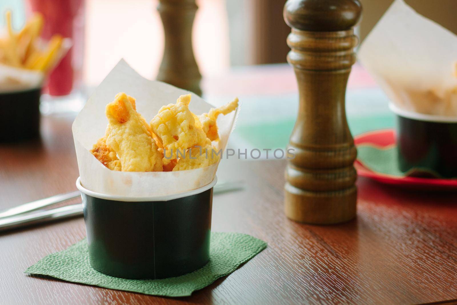 Pakora rolled to parchment in a black cup, over a wooden table, great image for your needs.