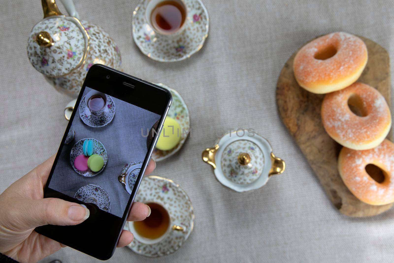 Top view picture of lady,blogger sitting in cafe and making photo with mobile of food, afternoon tea with doughnuts and macarons on the table high angle, food and social media concept by Annebel146