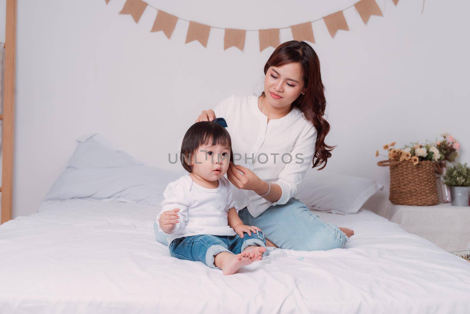 Mother combing her little daughters hair on the bed in bed room.