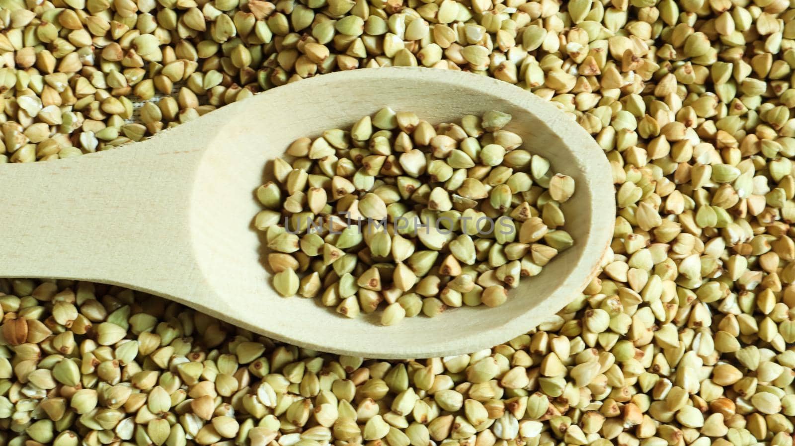 Buckwheat scattered background, raw green cereal in a wooden spoon. Healthy groats. Organic raw non-fried vegetarian food. The concept of a healthy and balanced diet. Diet product. healthy groats