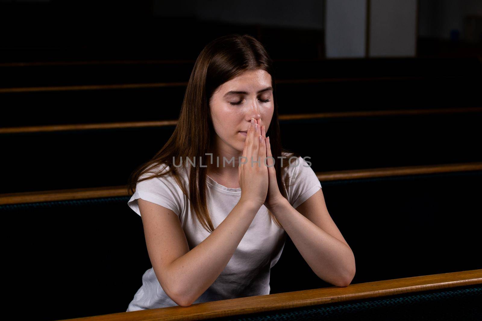 A Christian girl in white shirt is sitting and praying with humble heart in the church by lunarts